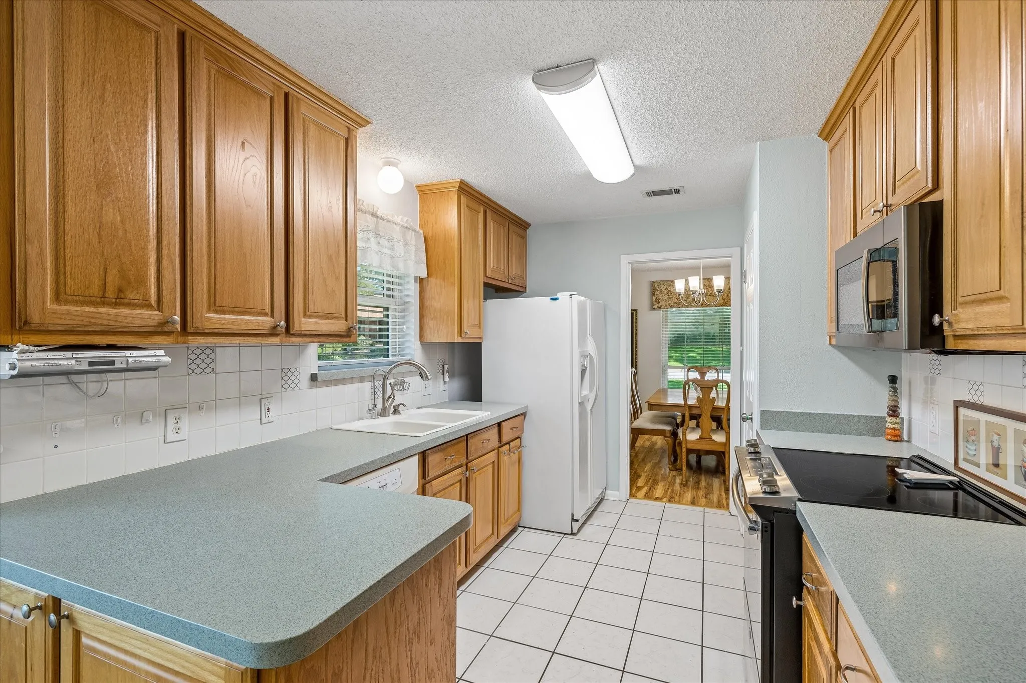 Galley kitchen featuring light wood cabinetry, light-toned countertops, and a white tile flooring