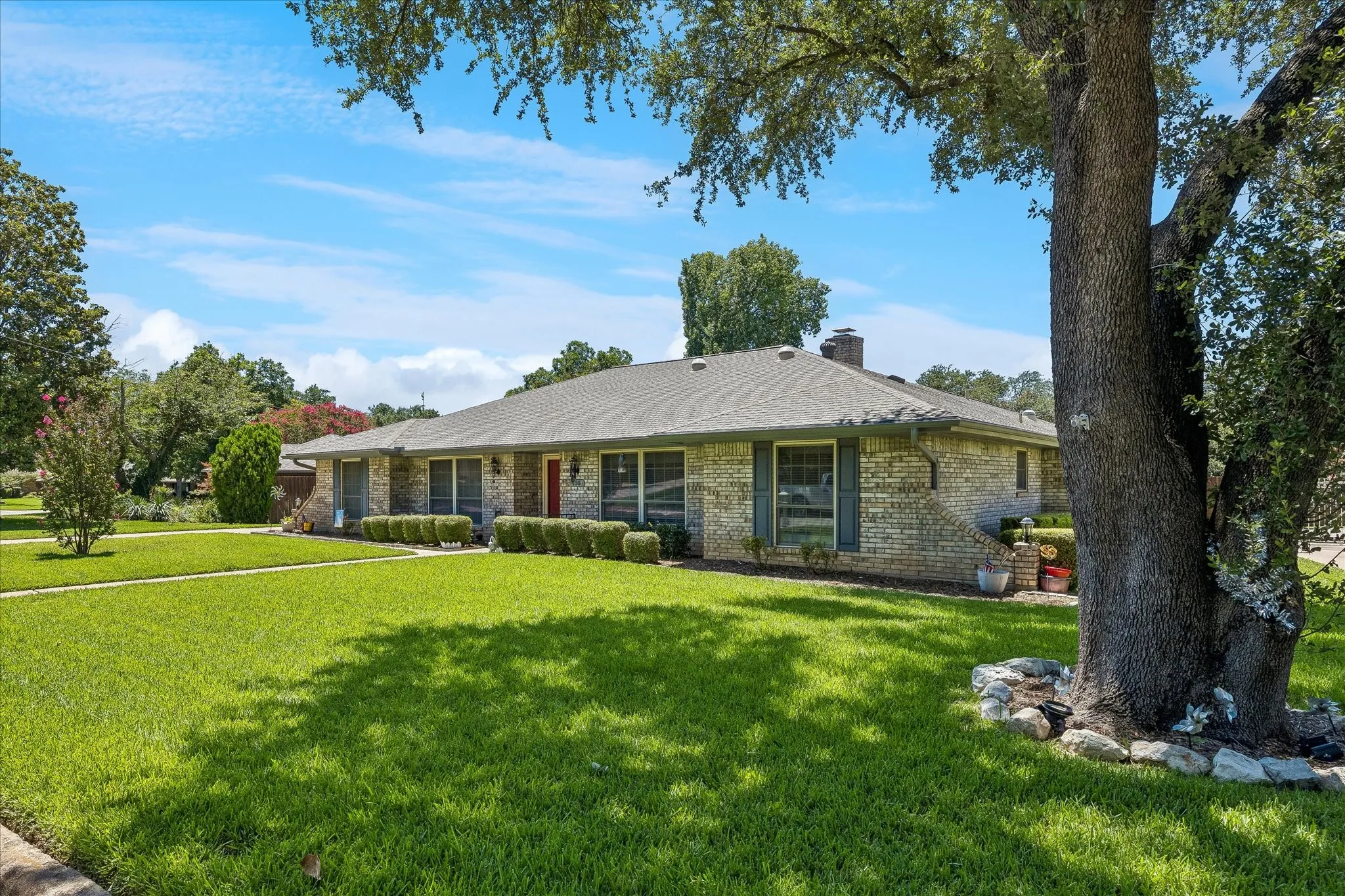 Charming brick ranch home set on expansive manicured grounds featuring mature shade trees, lush lawn, and established landscaping