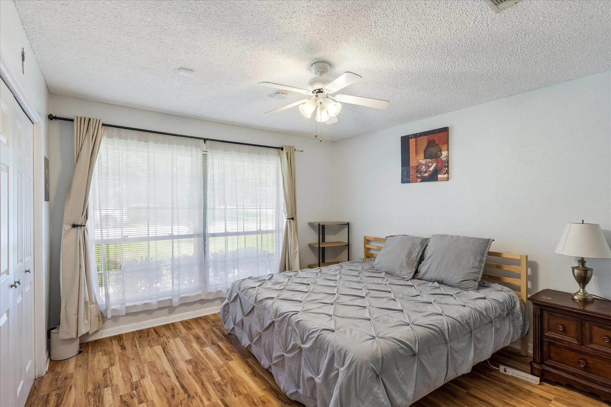 Bright master bedroom with sliding glass doors opening to natural light, wood-finish flooring throughout, and ceiling fan with integrated lighting