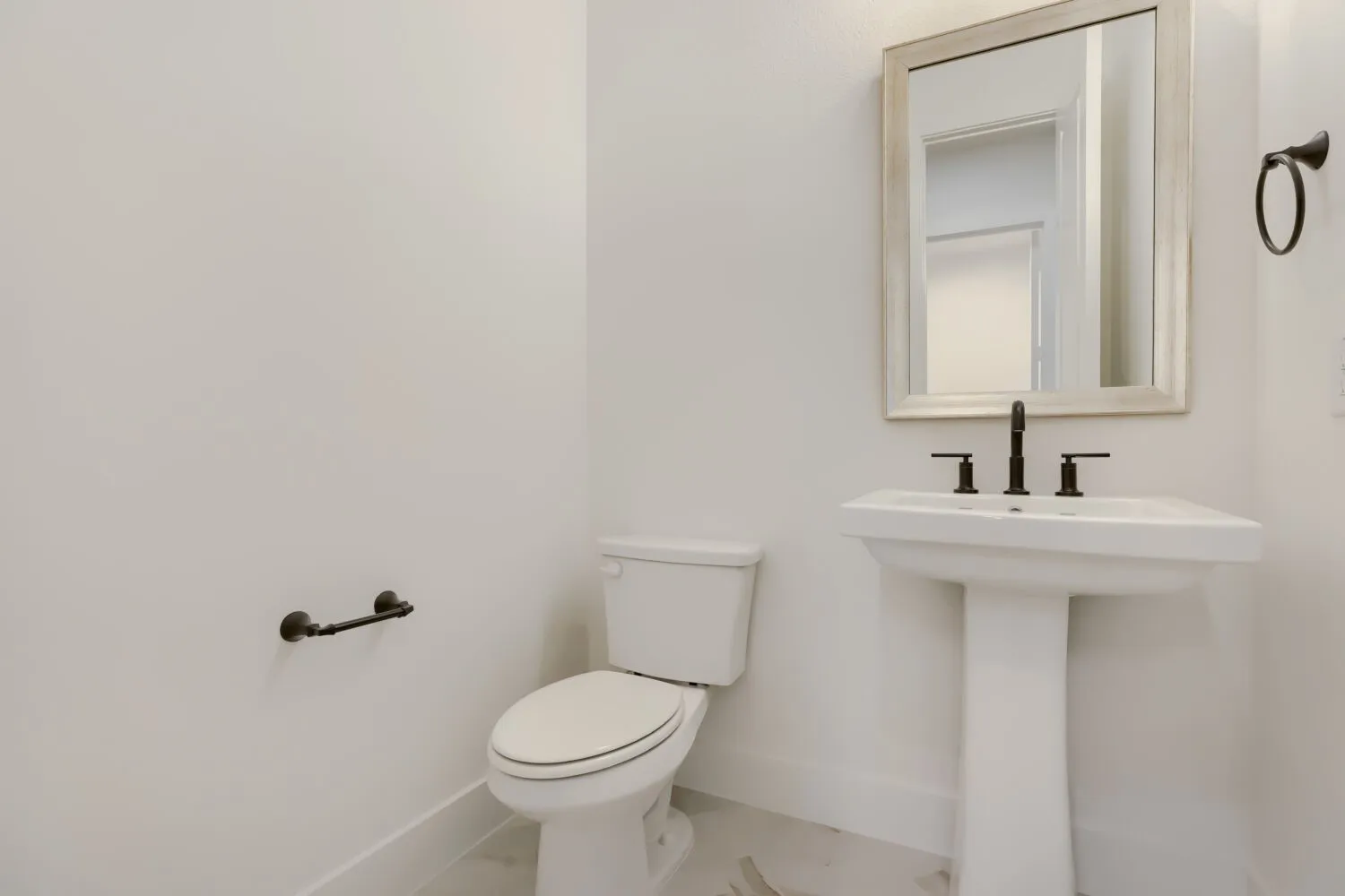 White pedestal sink with matte black fixtures and a framed mirror