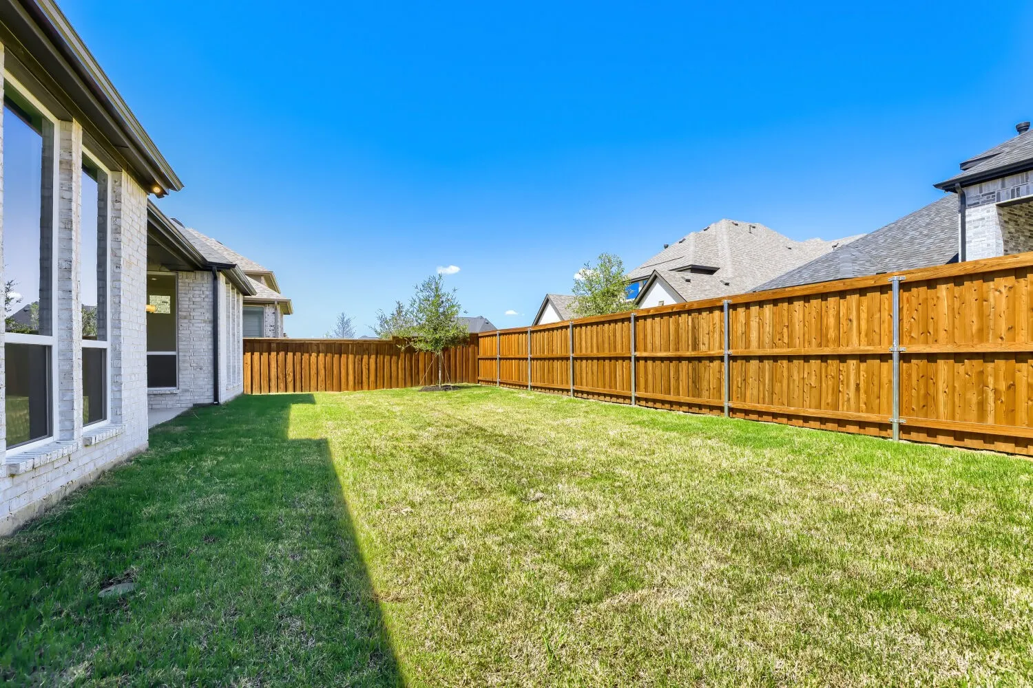 Expansive grass lawn bordered by a wood privacy fence and a white brick exterior