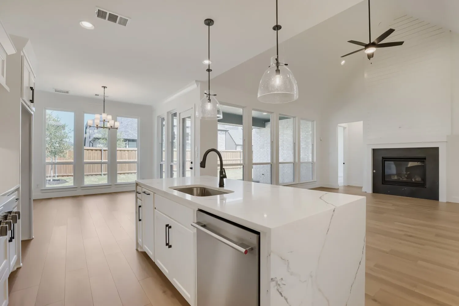 Contemporary kitchen featuring a large waterfall-edge island with quartz countertops, stainless steel appliances including a built-in dishwasher, and a matte black gooseneck faucet