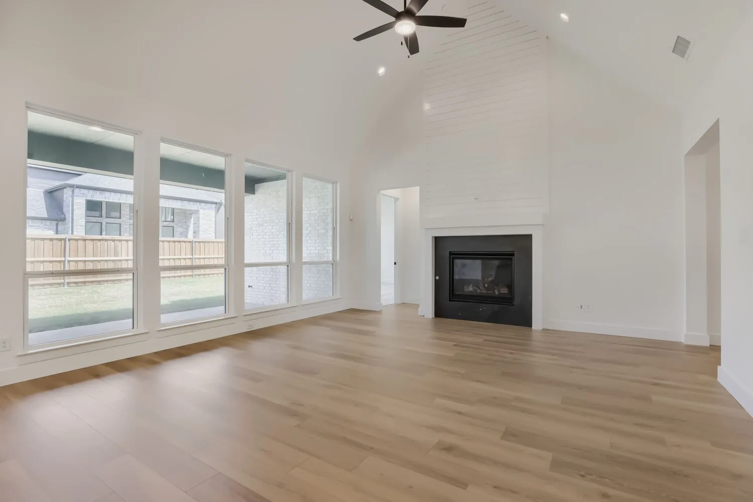 Vaulted ceiling with a ceiling fan and recessed lighting, modern fireplace with a dark surround, light wood-finish flooring, and a wall of windows