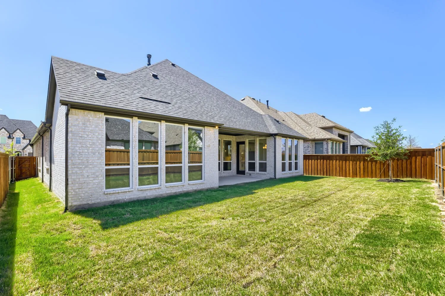 Expansive backyard featuring a manicured lawn, full privacy fencing, and a covered patio area