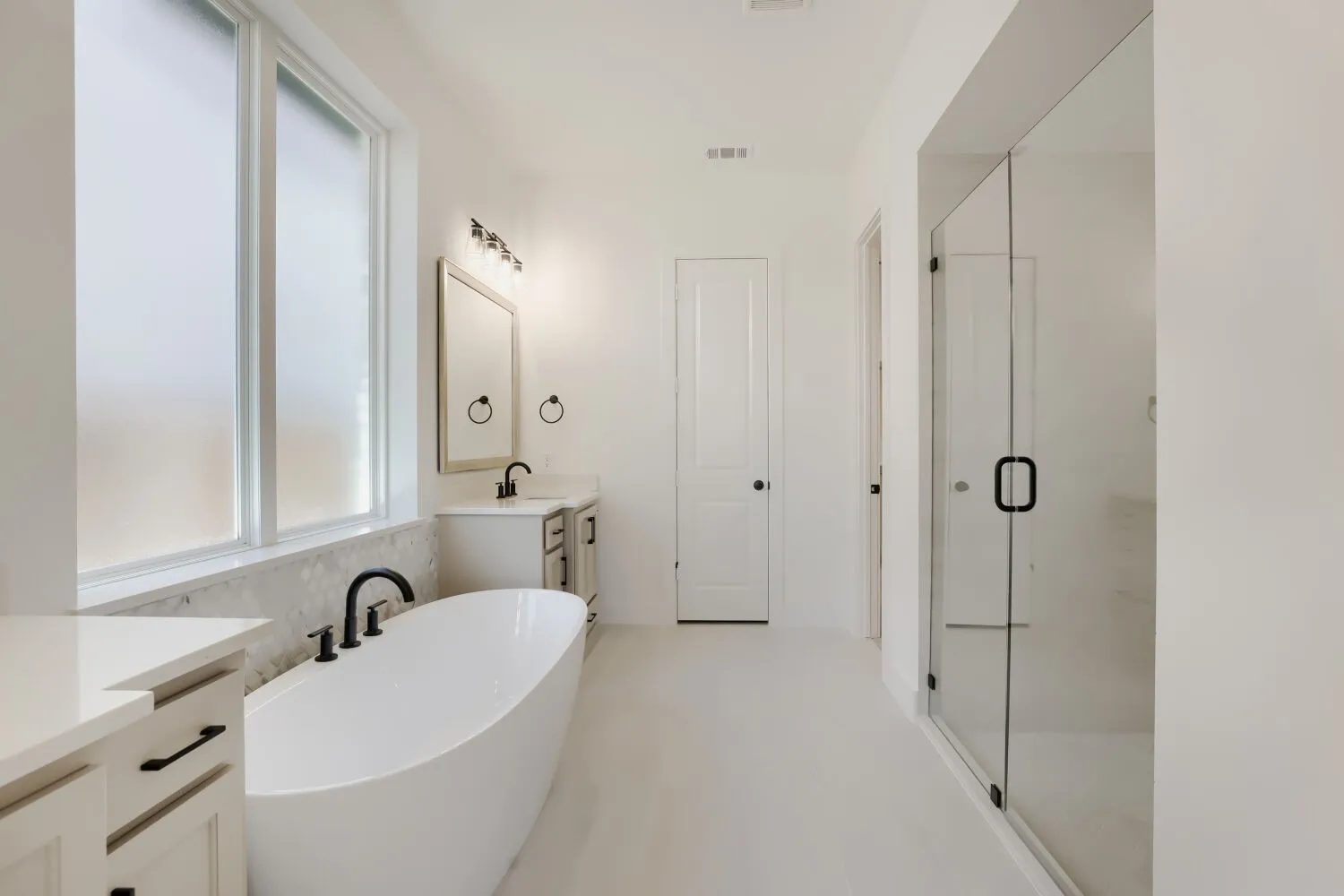 Freestanding soaking tub with matte black fixtures, dual vanities with integrated sinks, and a frameless glass shower enclosure