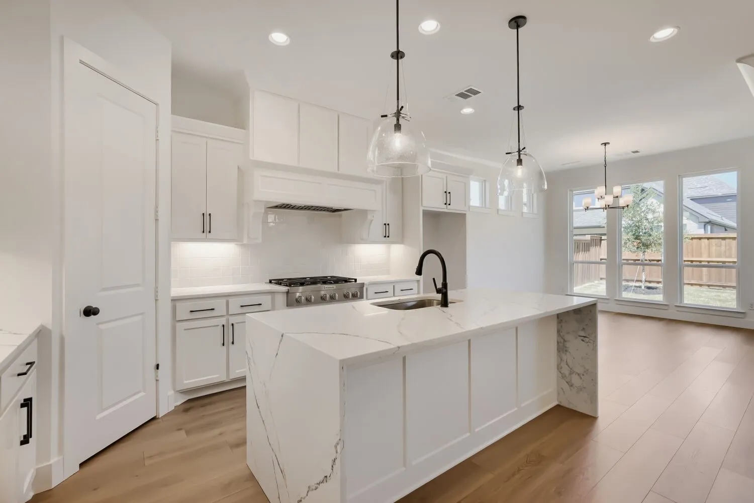 Kitchen featuring a large island with a waterfall countertop, pendant lighting, professional-grade range, white cabinetry, and wood-finish flooring
