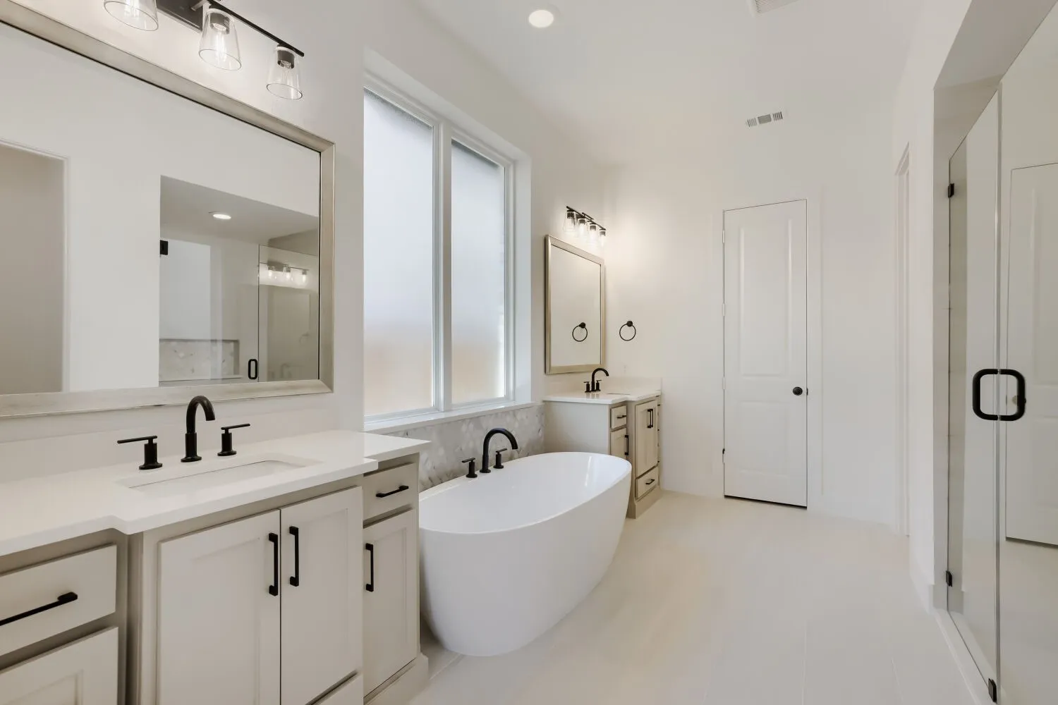 Dual vanities with undermount sinks, a freestanding soaking tub, a separate glass-enclosed shower, and frosted window panes