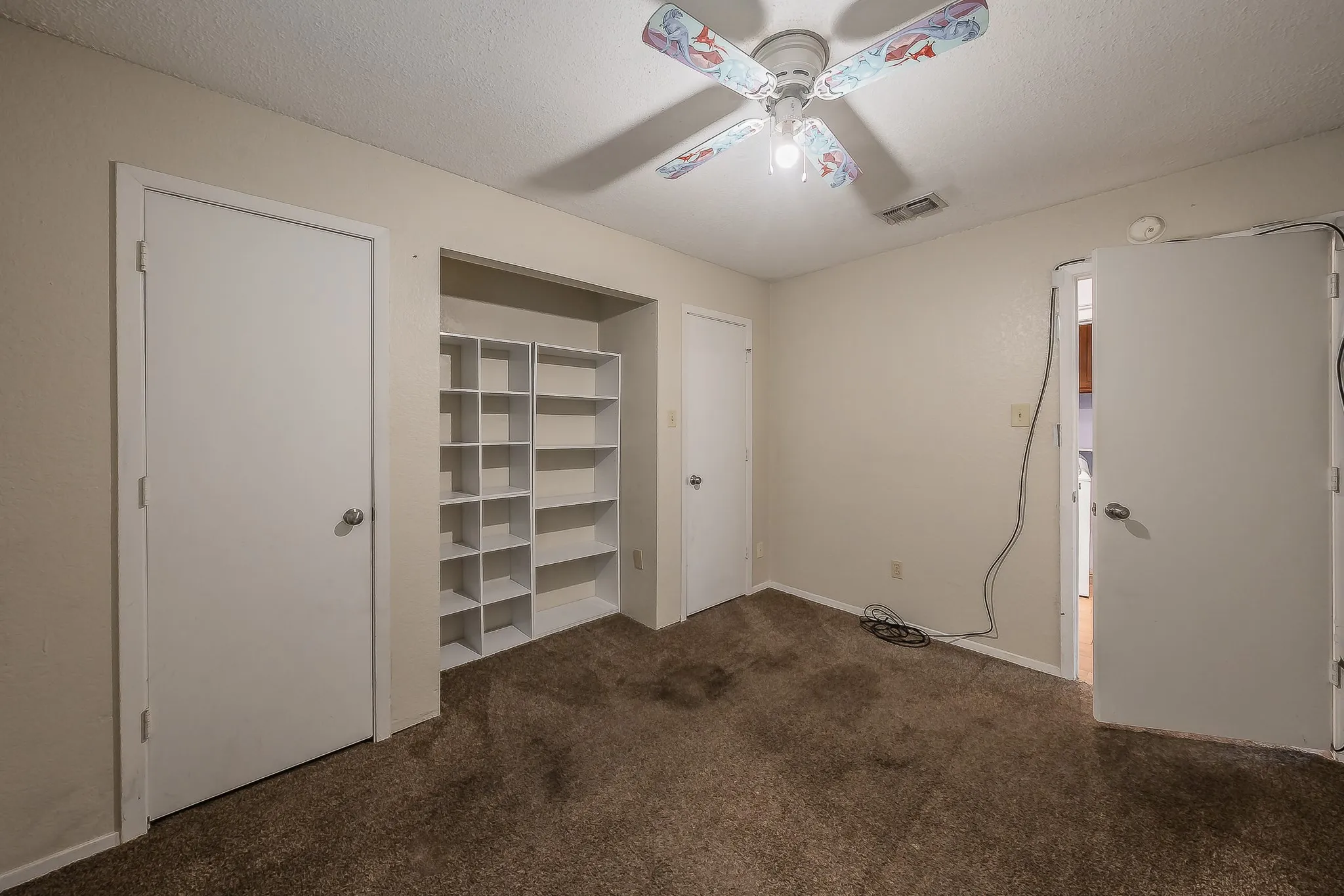 Carpeted room featuring a ceiling fan with light fixture, built-in shelving, and white interior doors