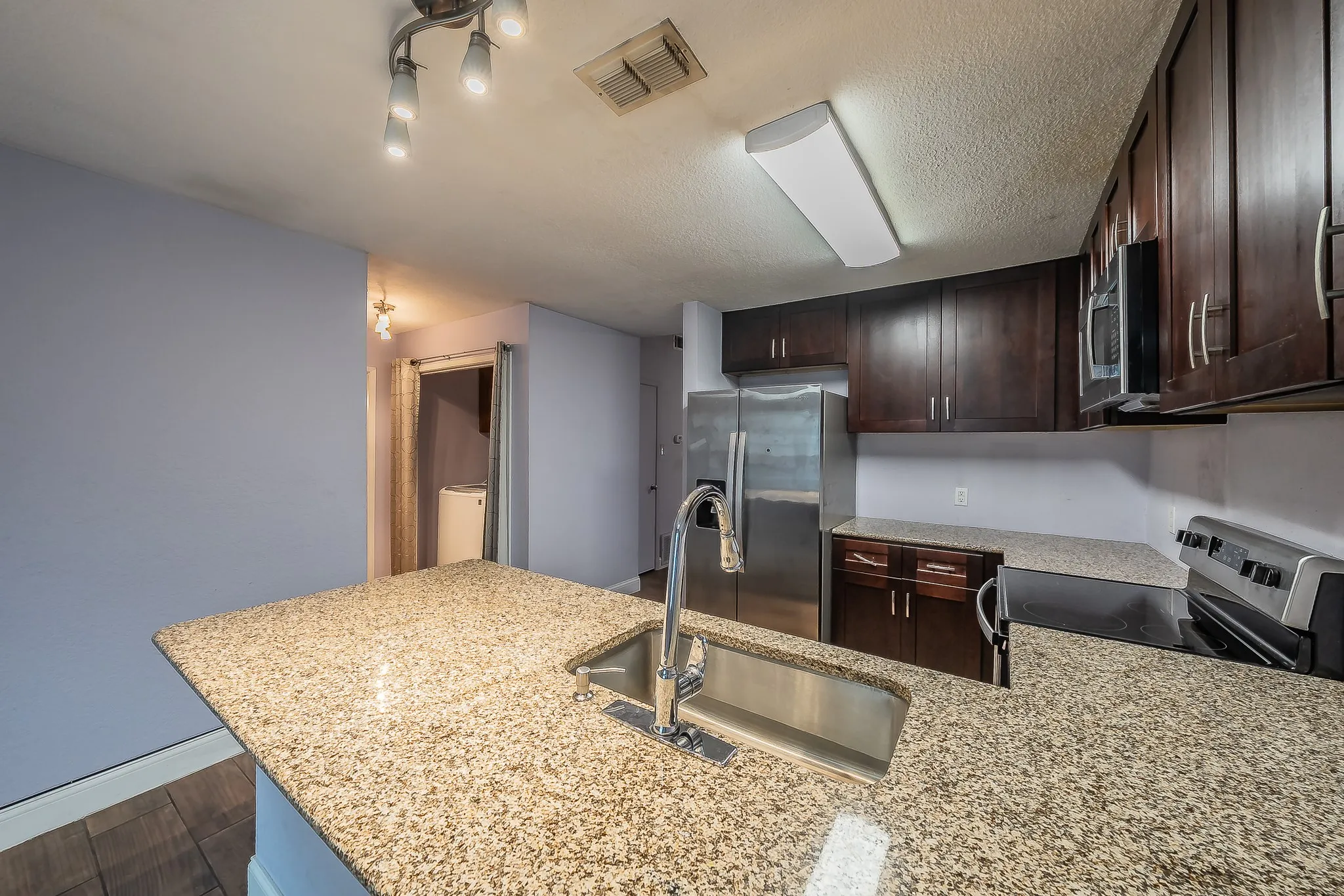Kitchen featuring granite-style countertops, dark wood cabinetry, a stainless-steel sink with a gooseneck faucet, and stainless-steel appliances
