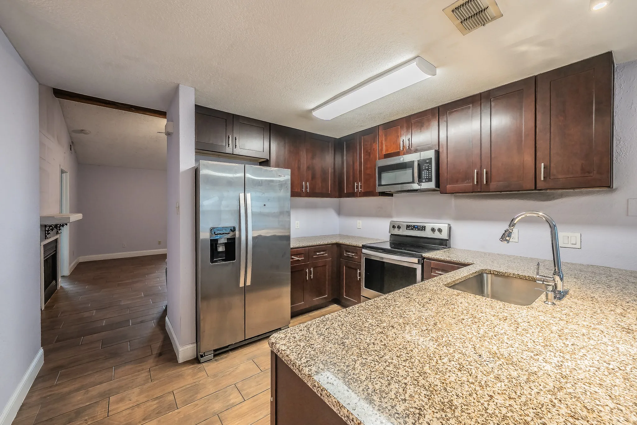 Kitchen featuring wood-finish flooring, dark wood cabinetry, granite-style countertops, and stainless steel appliances