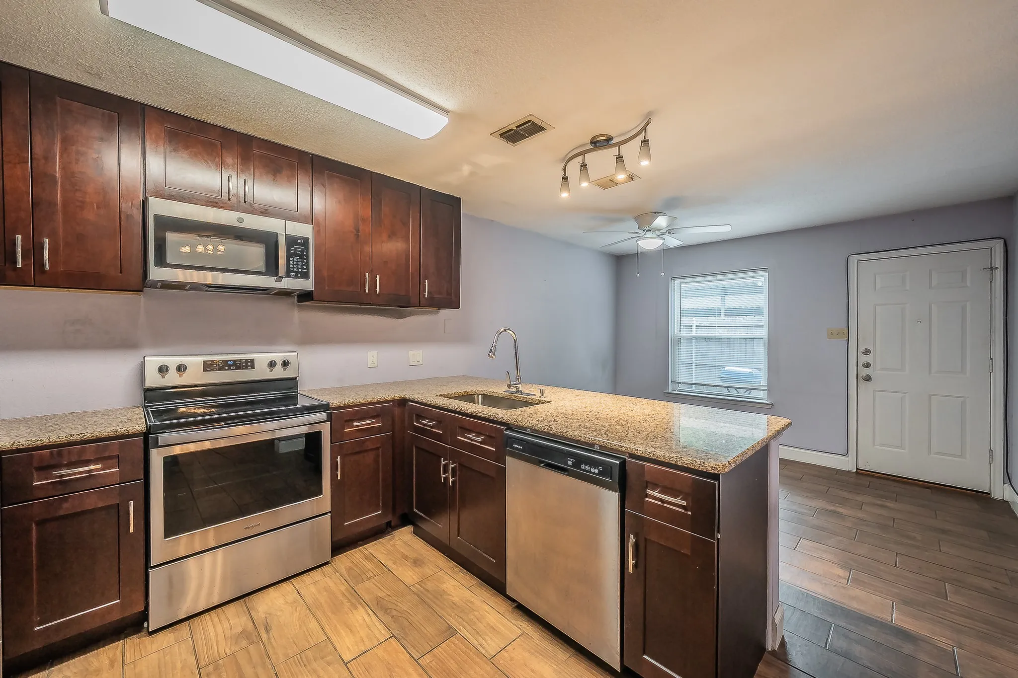 Kitchen featuring dark wood-finish cabinetry, stainless steel appliances, and a peninsula with a stone-finish countertop