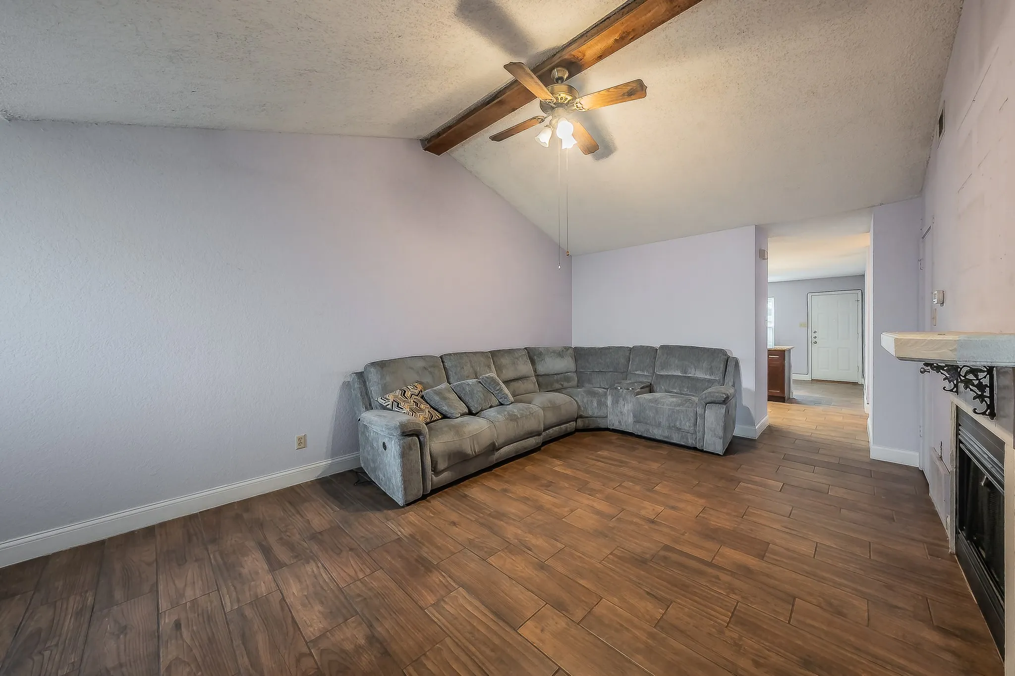 Spacious living area featuring wood-finish flooring, vaulted ceilings with exposed wood beams, and a ceiling fan