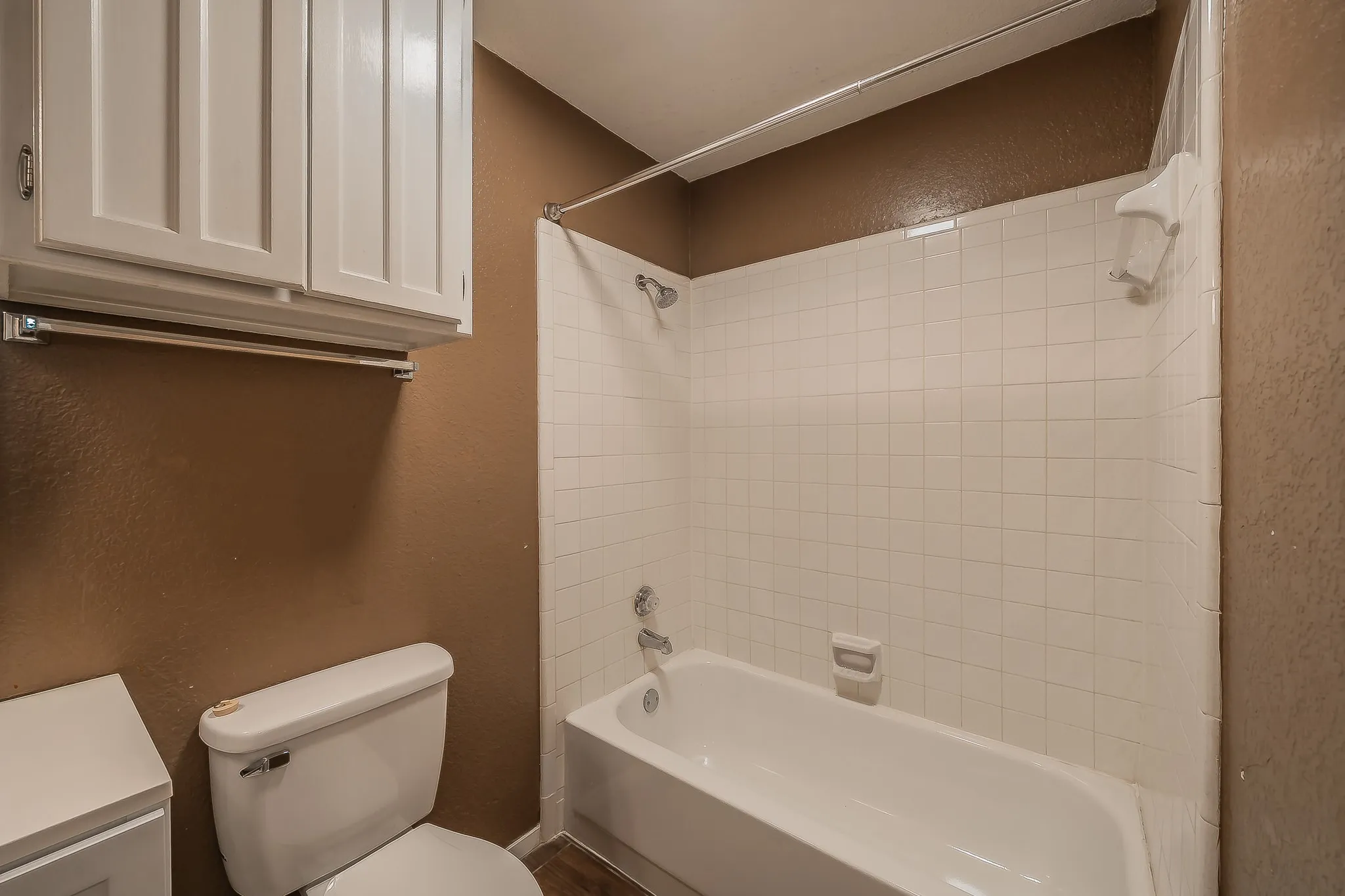 Bathroom featuring a white porcelain toilet, white overhead cabinetry with brushed nickel hardware, and a tub-shower combination with white subway tile surround