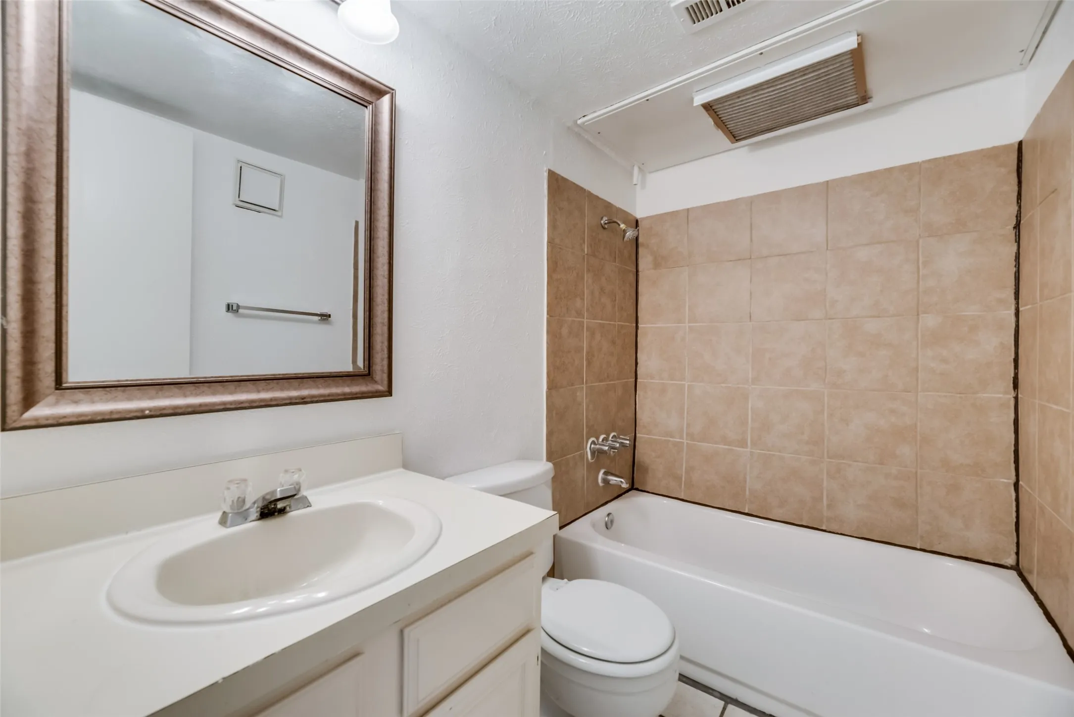 Full bathroom featuring oversized vanity, tiled shower / bath combo, toilet, and a textured ceiling