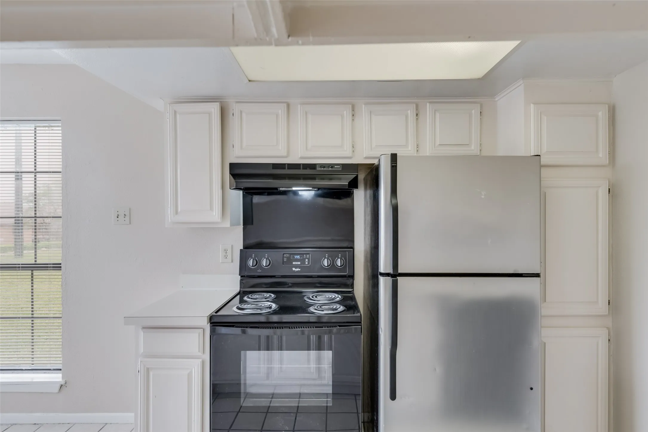 Kitchen featuring white cabinets, black range with electric cooktop, stainless steel fridge, and plenty of natural light