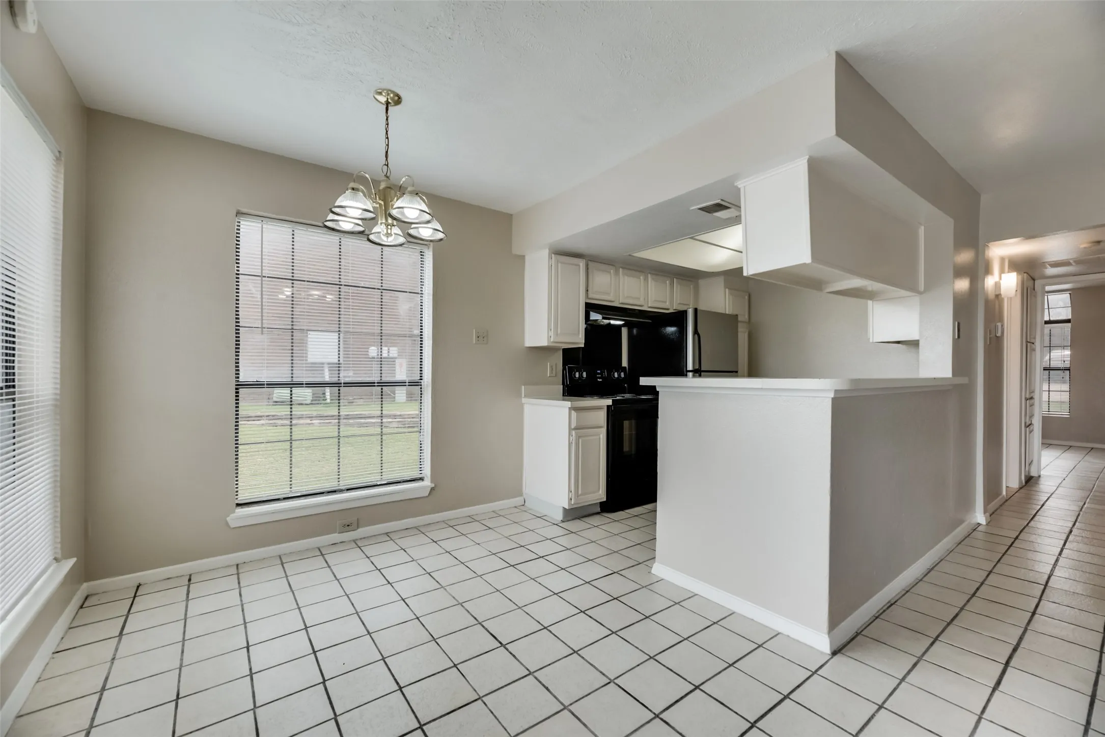 Kitchen with pendant lighting, white cabinets, light tile flooring, black range with electric cooktop, and a notable chandelier