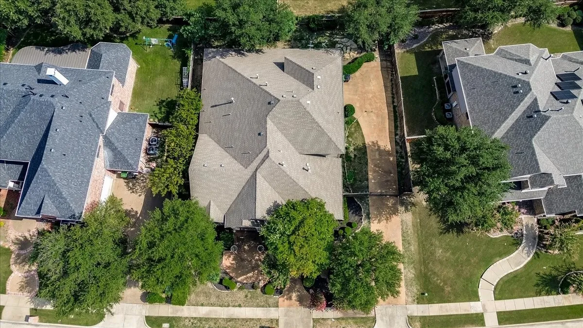 Aerial view showcasing this residence featuring a spacious roofline with multiple architectural planes, mature landscaping with established trees throughout the lot, and manicured lawn areas