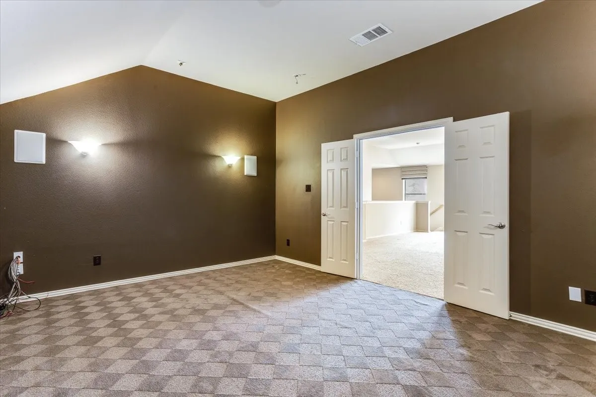 Spacious bonus room featuring vaulted ceilings, a geometric patterned carpet, and dual white six-panel doors opening to a carpeted landing