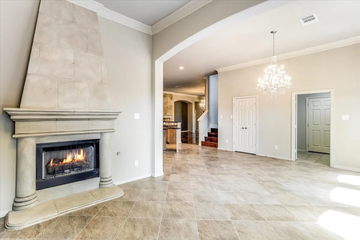 Tile-surround fireplace with a stone mantel, crown molding, a crystal chandelier, arched doorways, and tile flooring