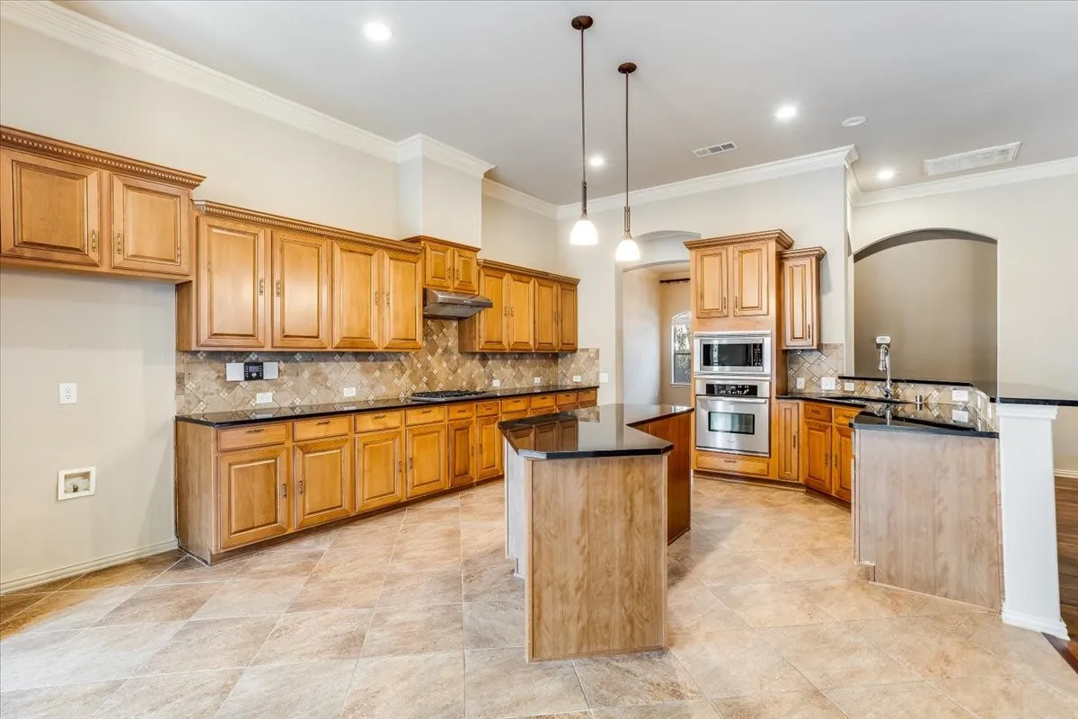 Spacious kitchen featuring extensive wood cabinetry, dark countertops, a large center island, built-in stainless steel appliances, and tile flooring