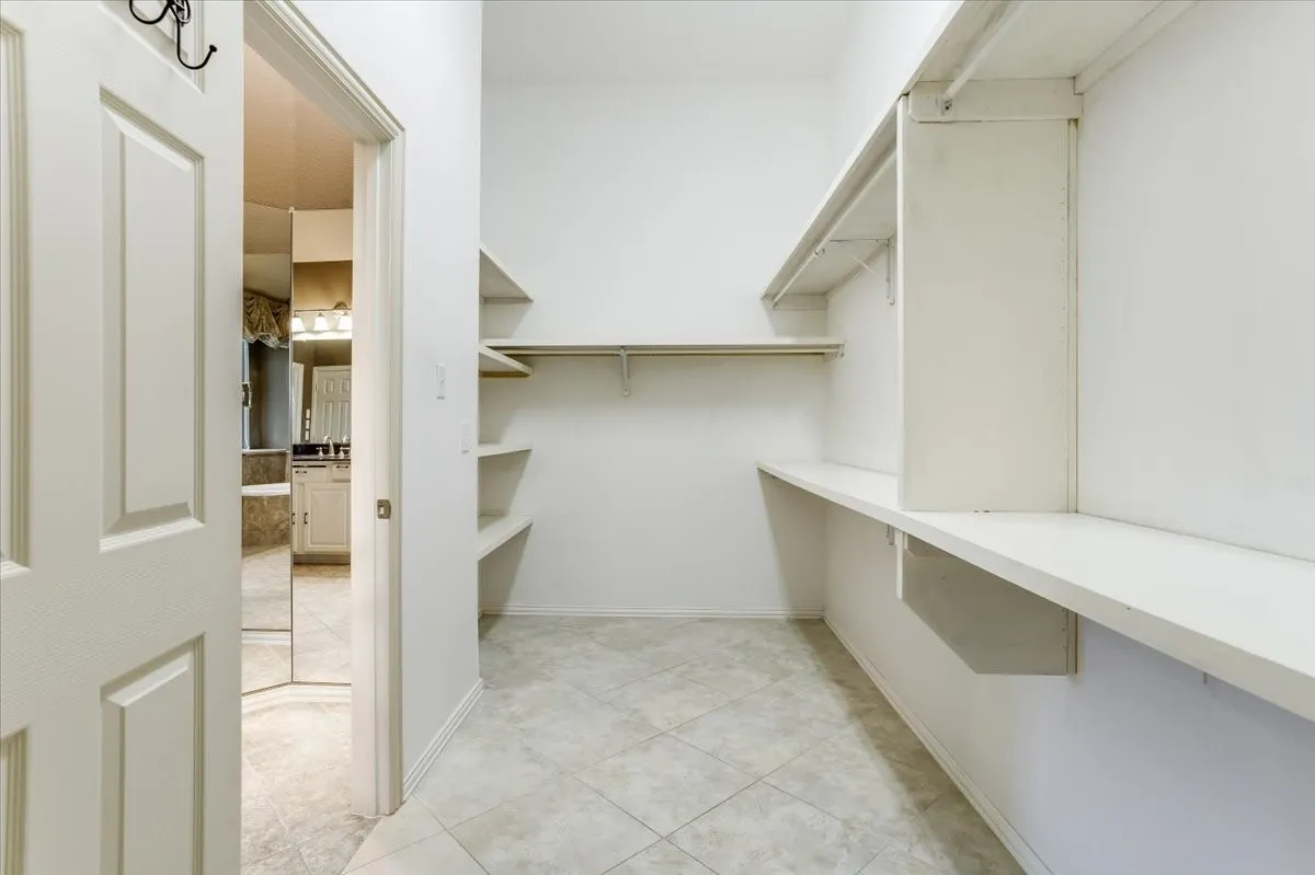 Spacious walk-in closet featuring built-in shelving, hanging rods, and light-toned tile flooring