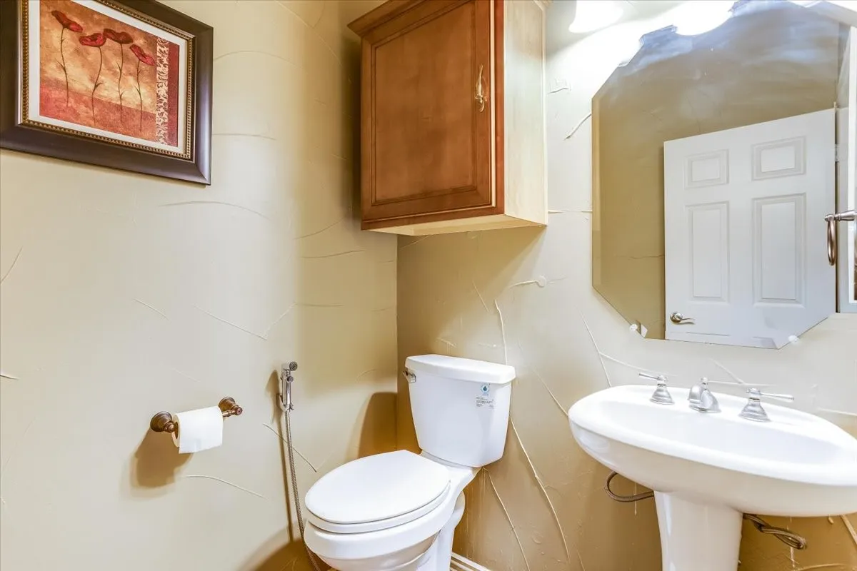 Pedestal sink with chrome faucet set, complemented by a white toilet and a wood-finish wall cabinet