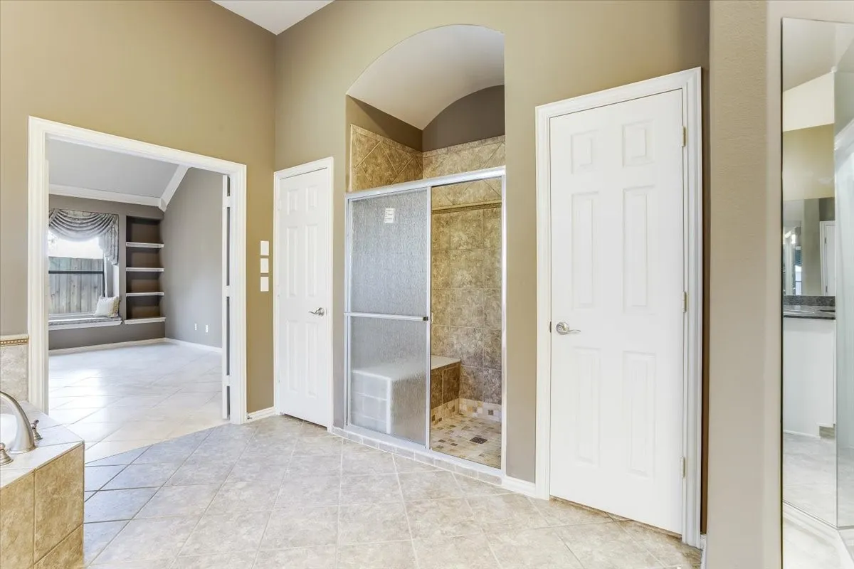 Spacious bathroom featuring large format floor tiles, a tiled walk-in shower with glass enclosure and built-in bench, and an adjacent soaking tub