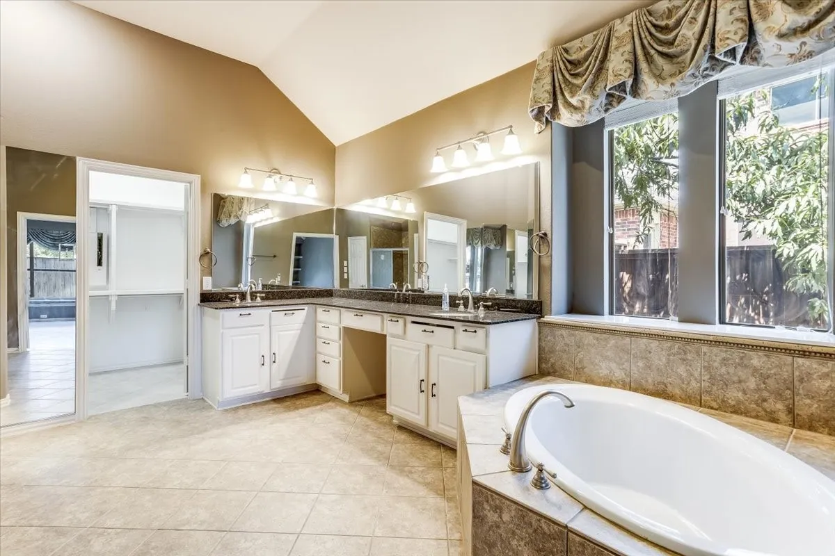 Luxurious primary bathroom featuring dual vanities with ample storage, illuminated mirrors, and quartz countertops