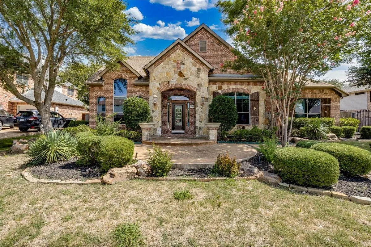 Two-story stone and brick exterior featuring an arched entryway, decorative transom window, and shuttered windows