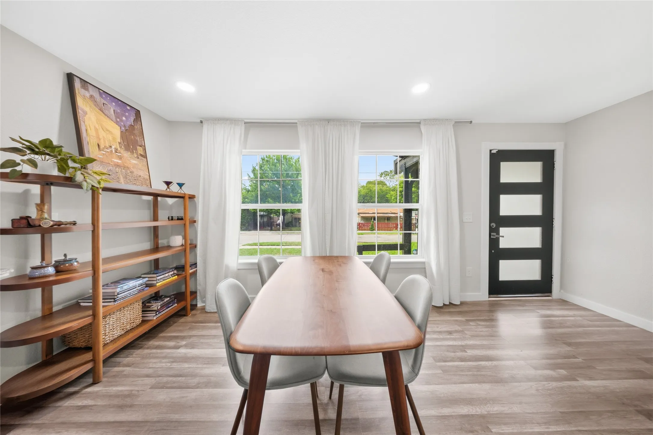 Elegant dining room showcasing a wood-finish dining table with mid-century modern seating, hardwood flooring, and abundant natural light from dual French doors