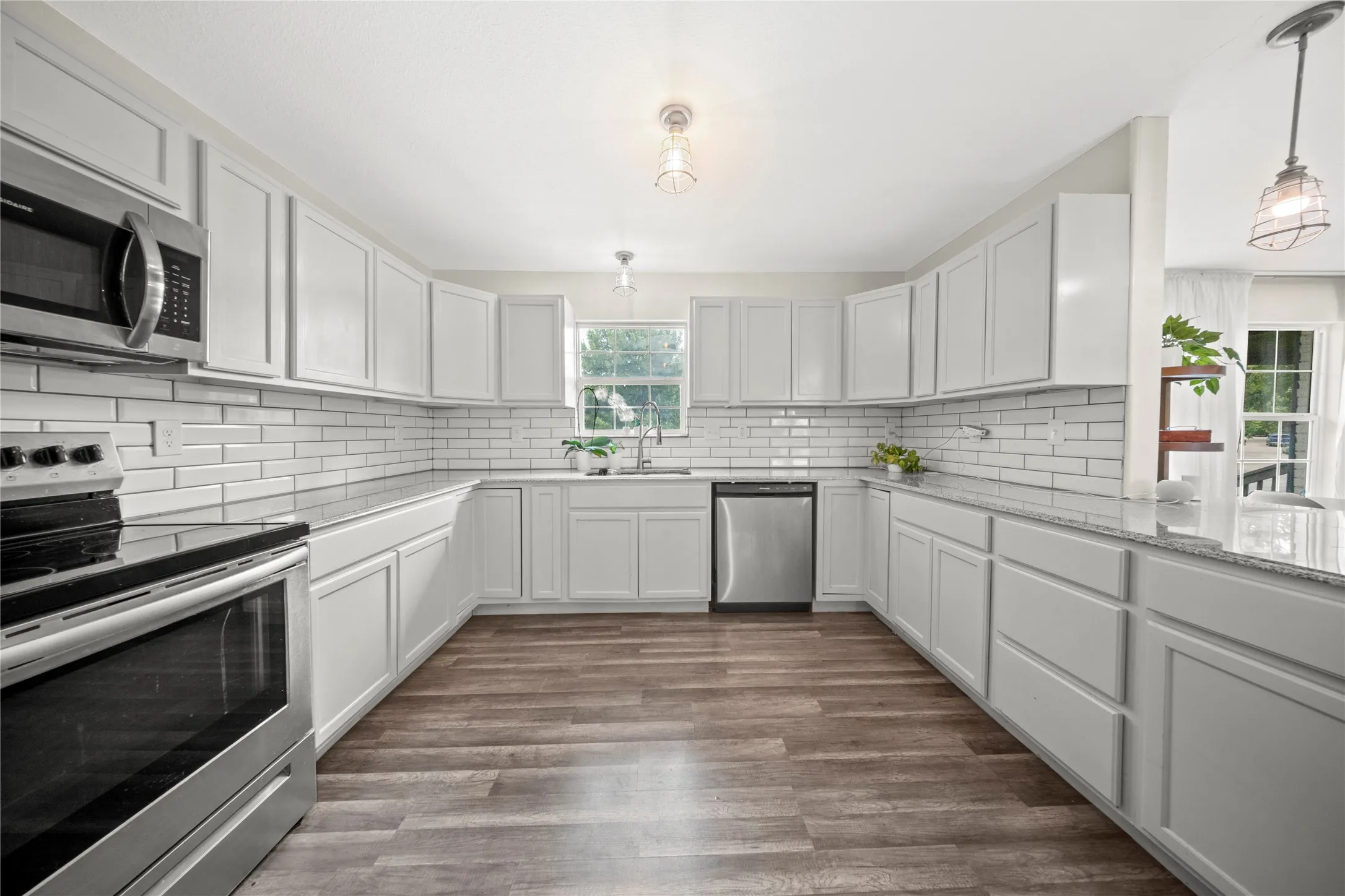 Modern kitchen featuring extensive white cabinetry, stainless steel appliances, white subway tile backsplash, granite countertops, and wood-finish flooring