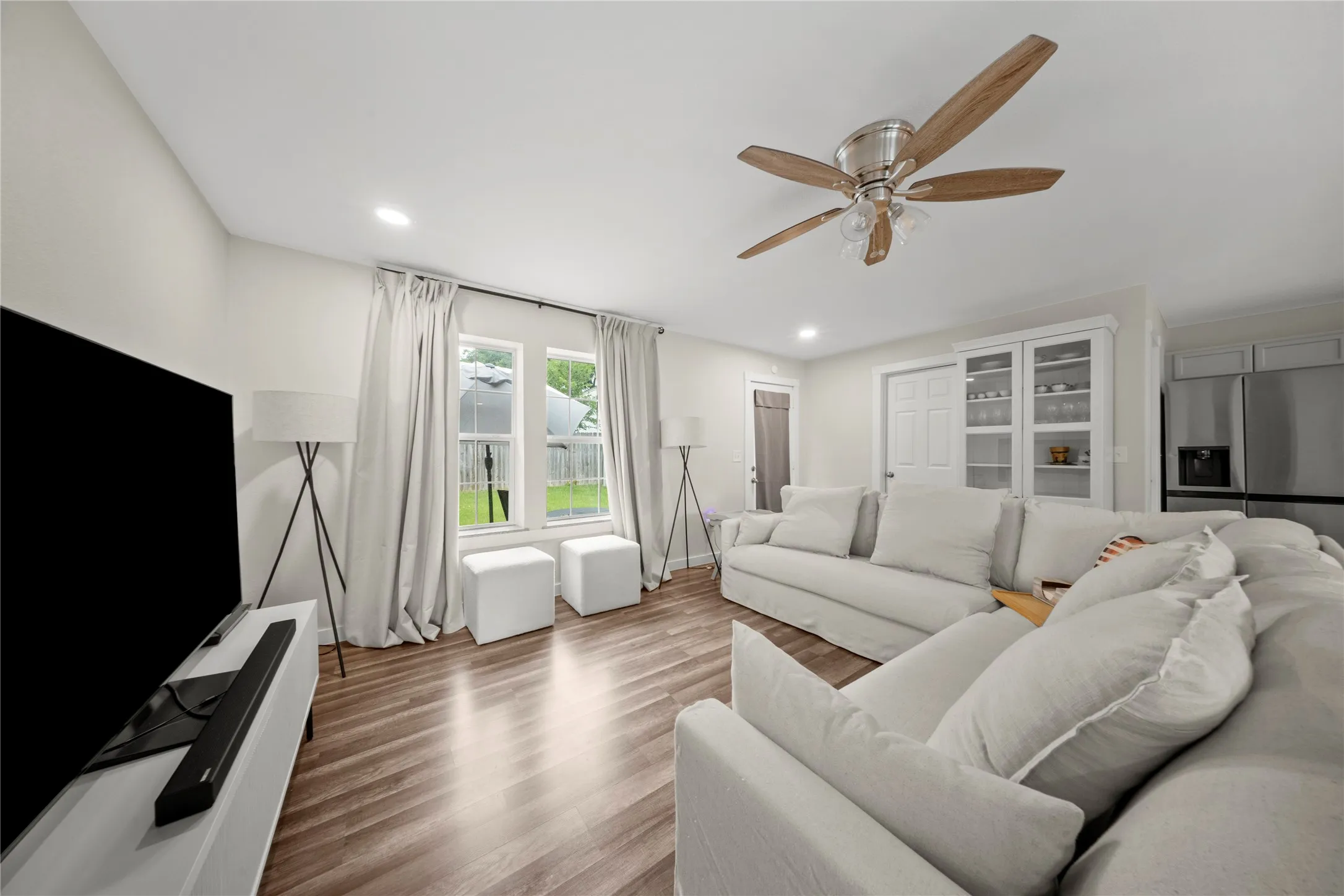 Spacious living area featuring wood-finish flooring, a ceiling fan with light fixture, and recessed lighting