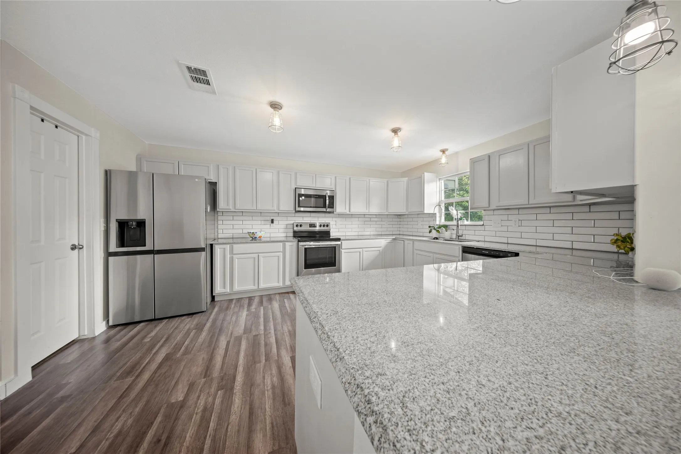 Kitchen featuring granite countertops, stainless steel appliances, white subway tile backsplash, white cabinetry, and wood-finish flooring