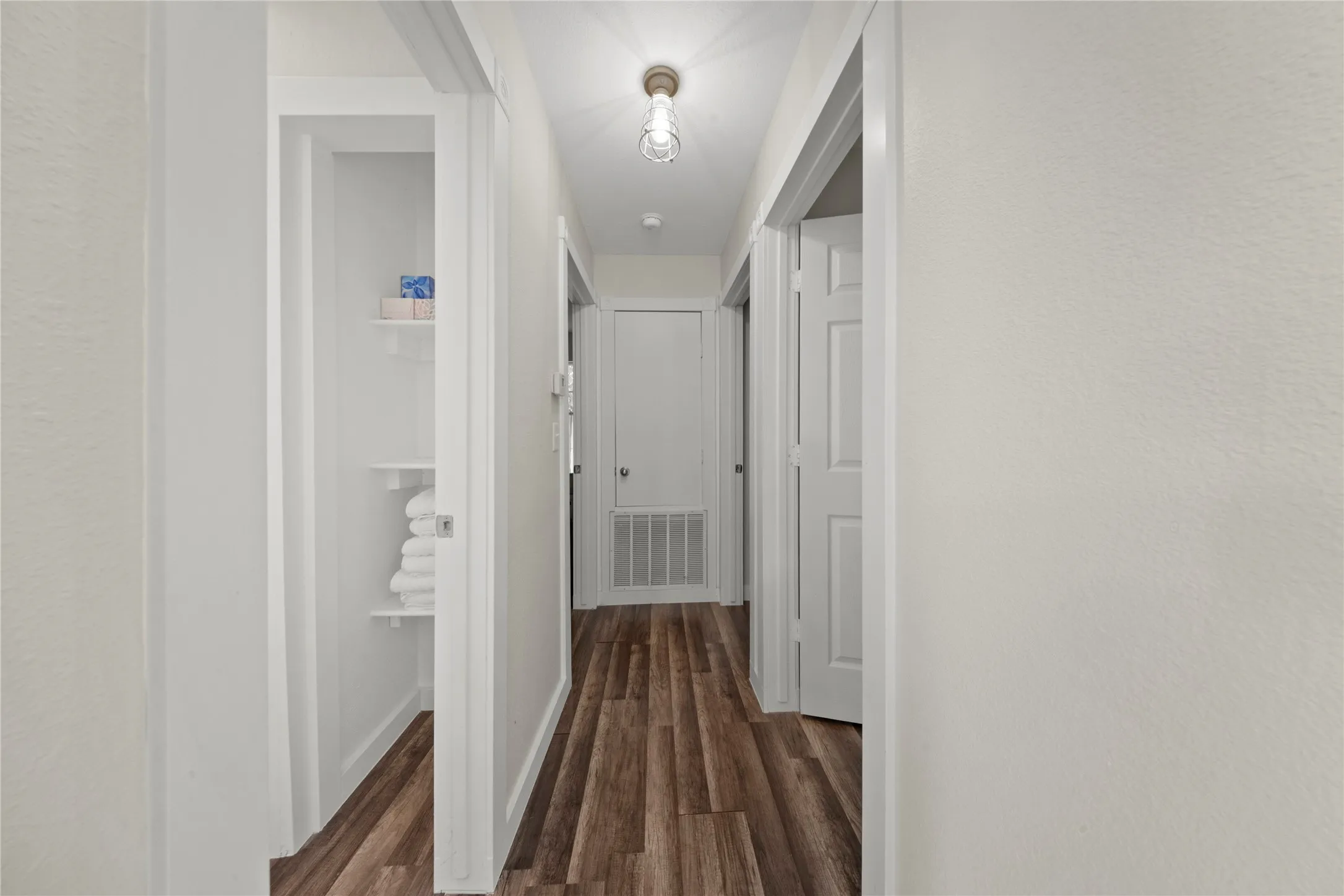 Hallway with wood-finish flooring, white walls, and a ceiling-mounted light fixture