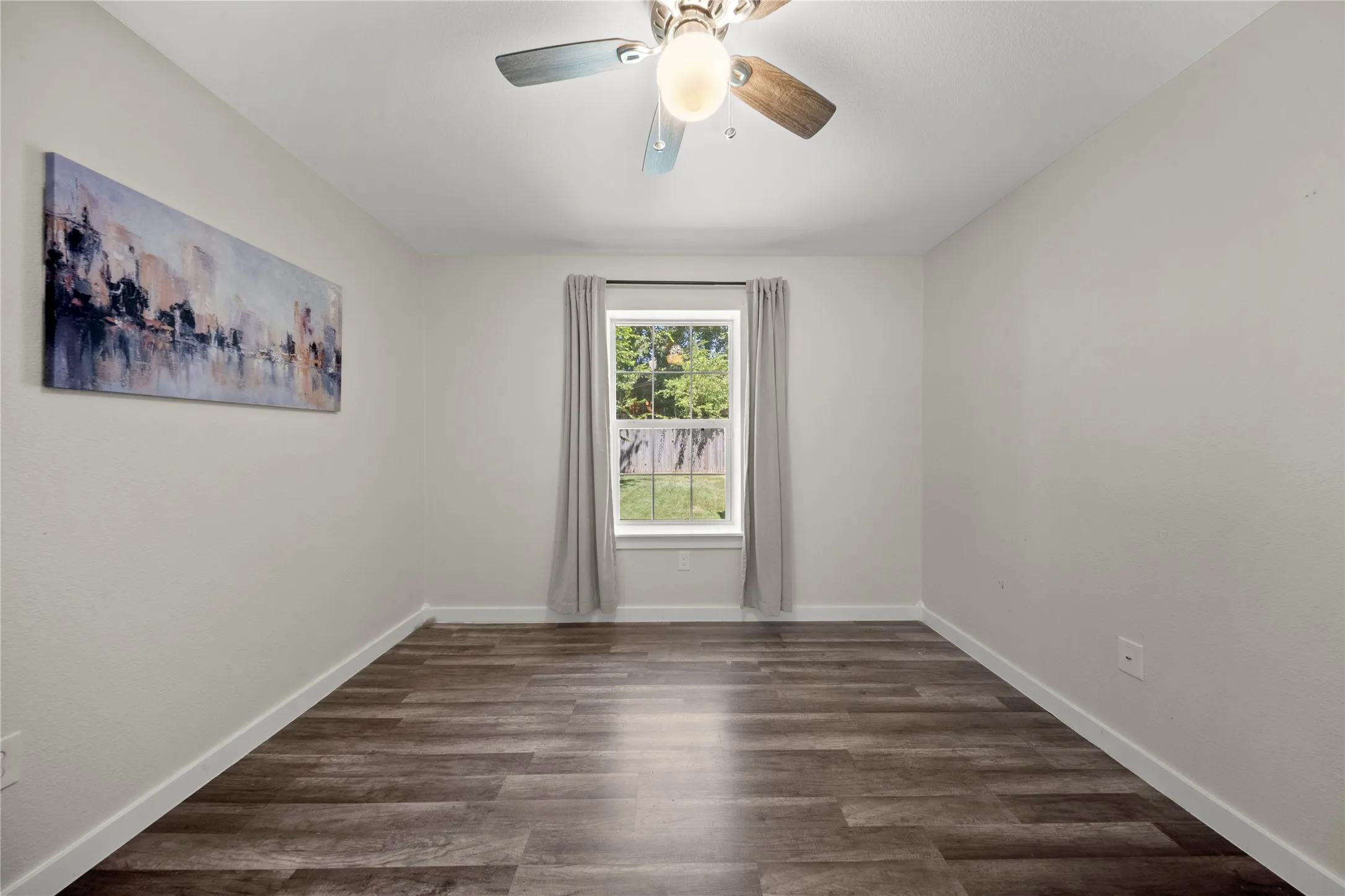Room featuring wood-finish flooring, a ceiling fan with integrated lighting, a window with exterior views, and neutral wall tones