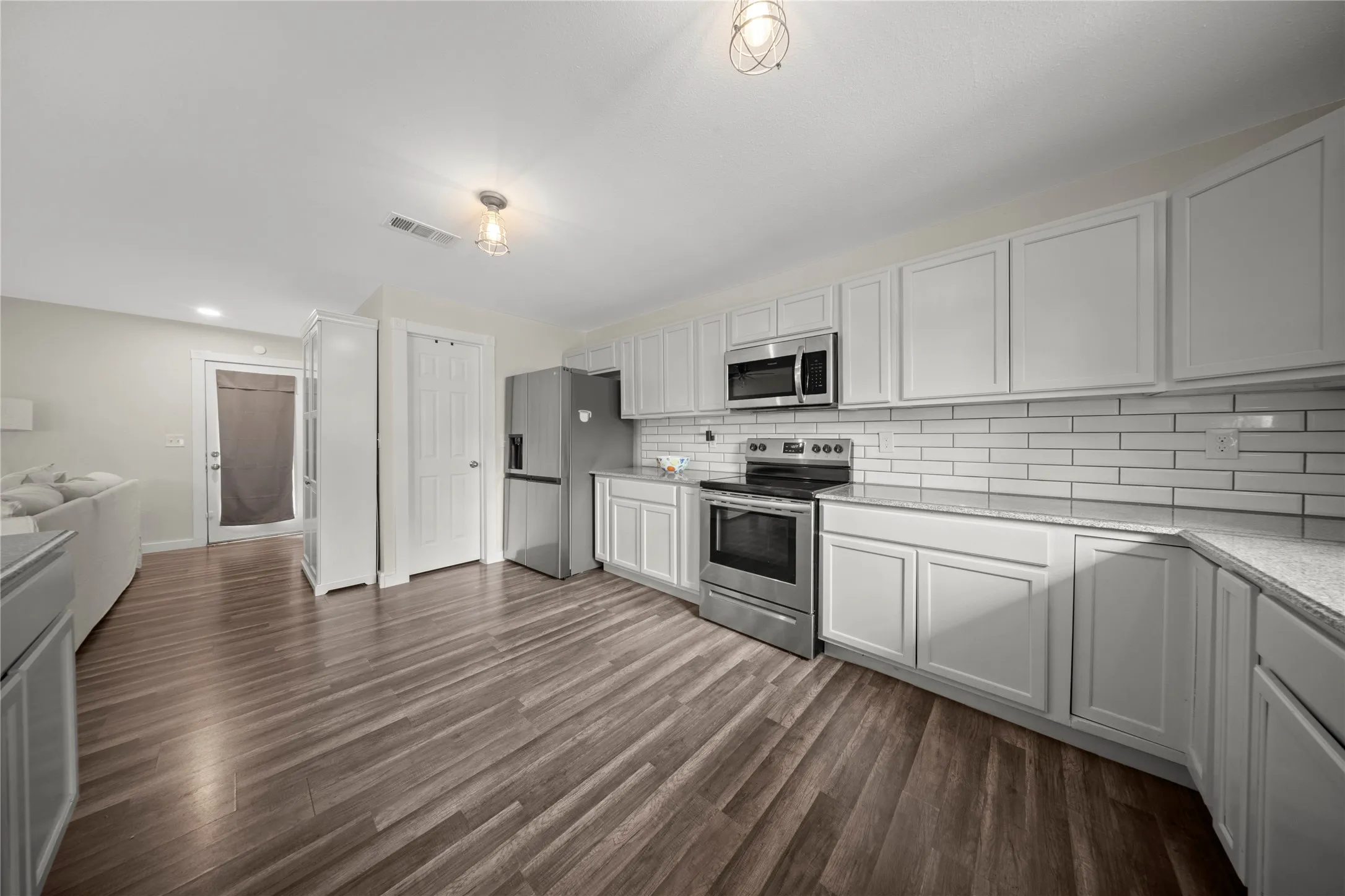 Kitchen featuring white shaker-style cabinetry, stainless steel appliances, subway tile backsplash, and light-toned countertops