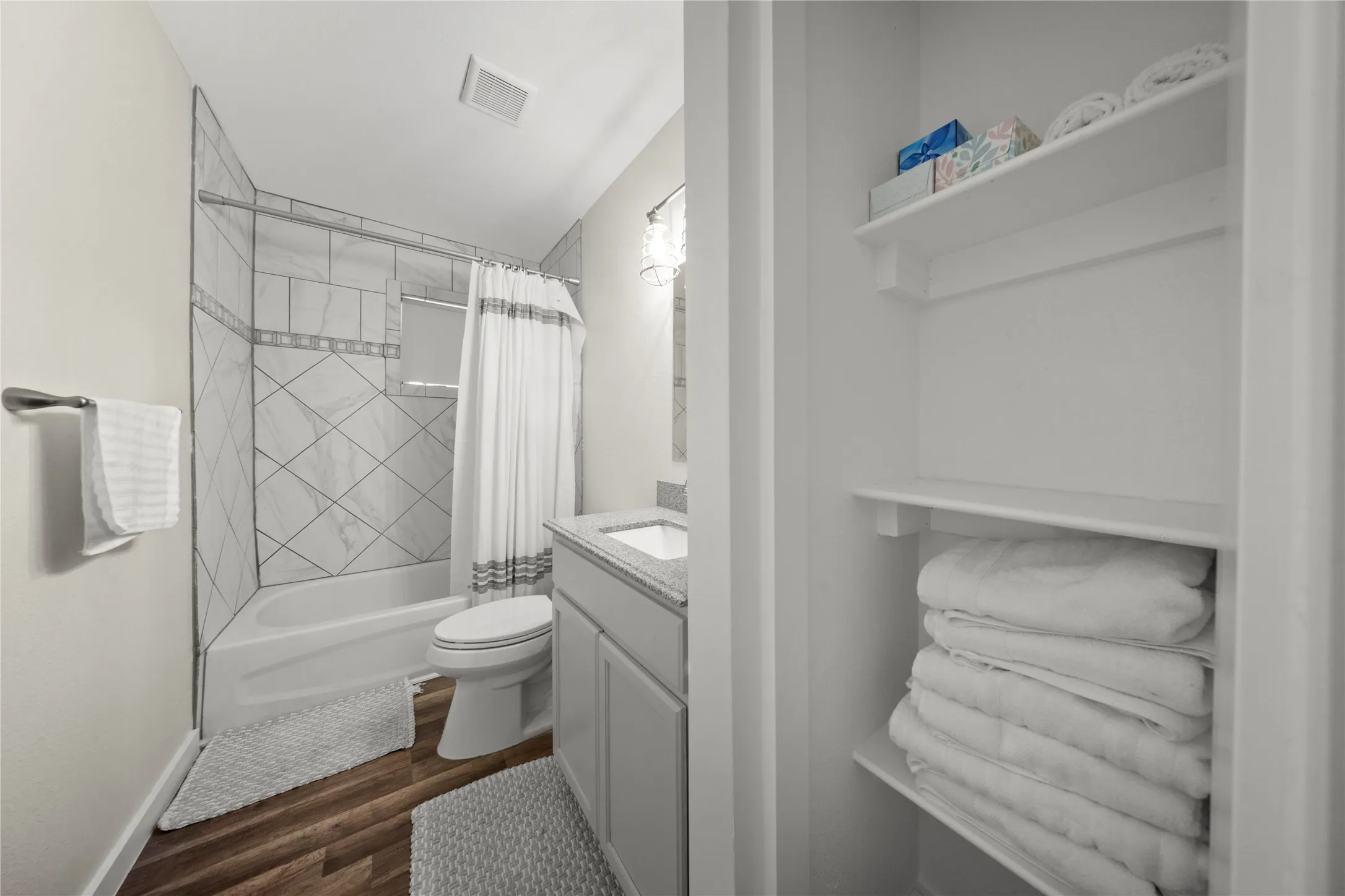 Bathroom featuring a white tub and shower combination with diagonal and horizontal tile work, a vanity with a light-colored countertop, and wood-finish flooring