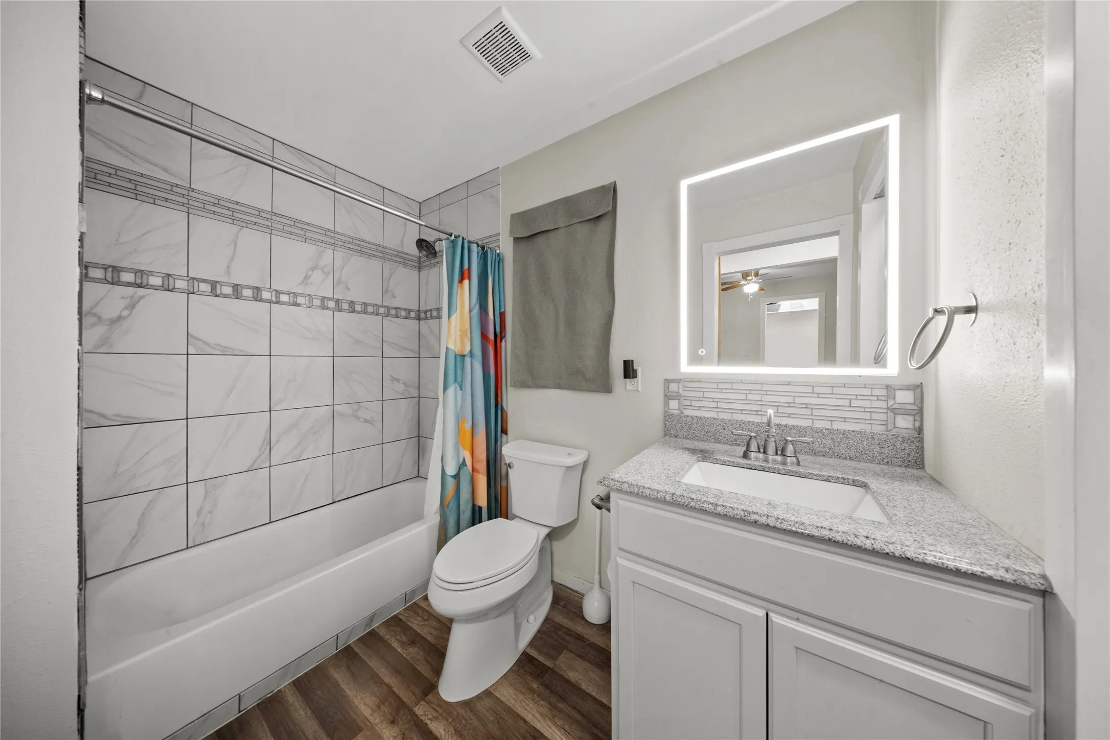 Full bathroom featuring a white tub-shower combination with marble-look tile surround and decorative accent banding