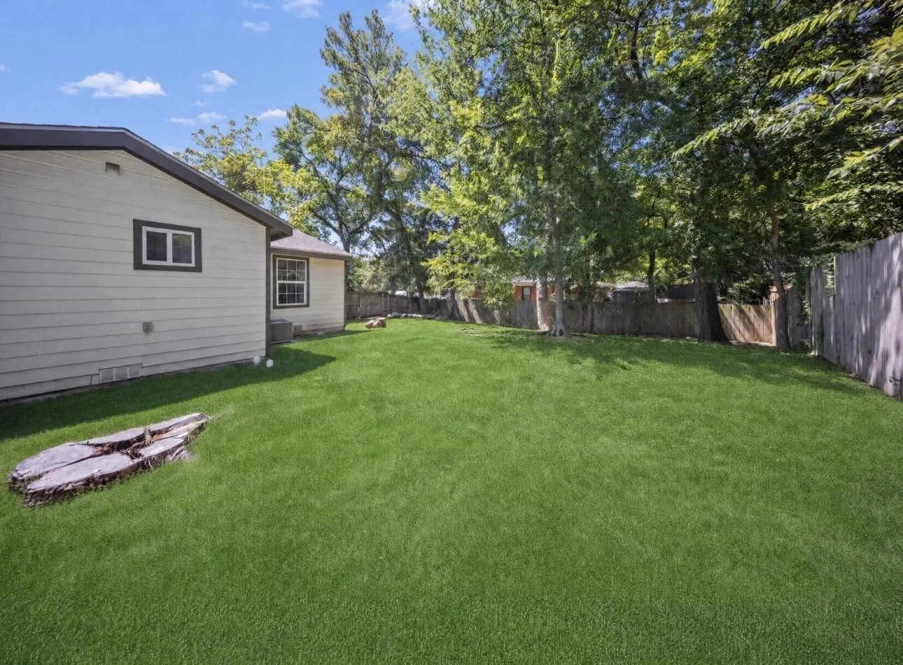 Spacious backyard featuring a lush lawn, mature trees providing shade, and a wood privacy fence