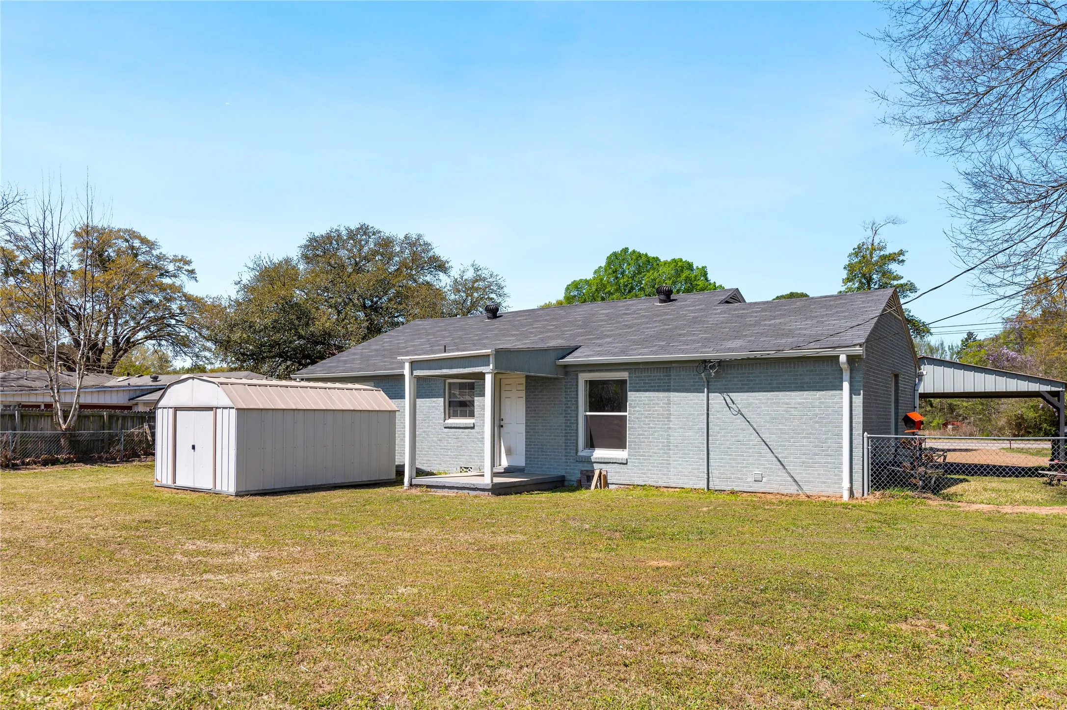 Expansive backyard featuring a detached storage shed, a covered carport, and a chain-link fence