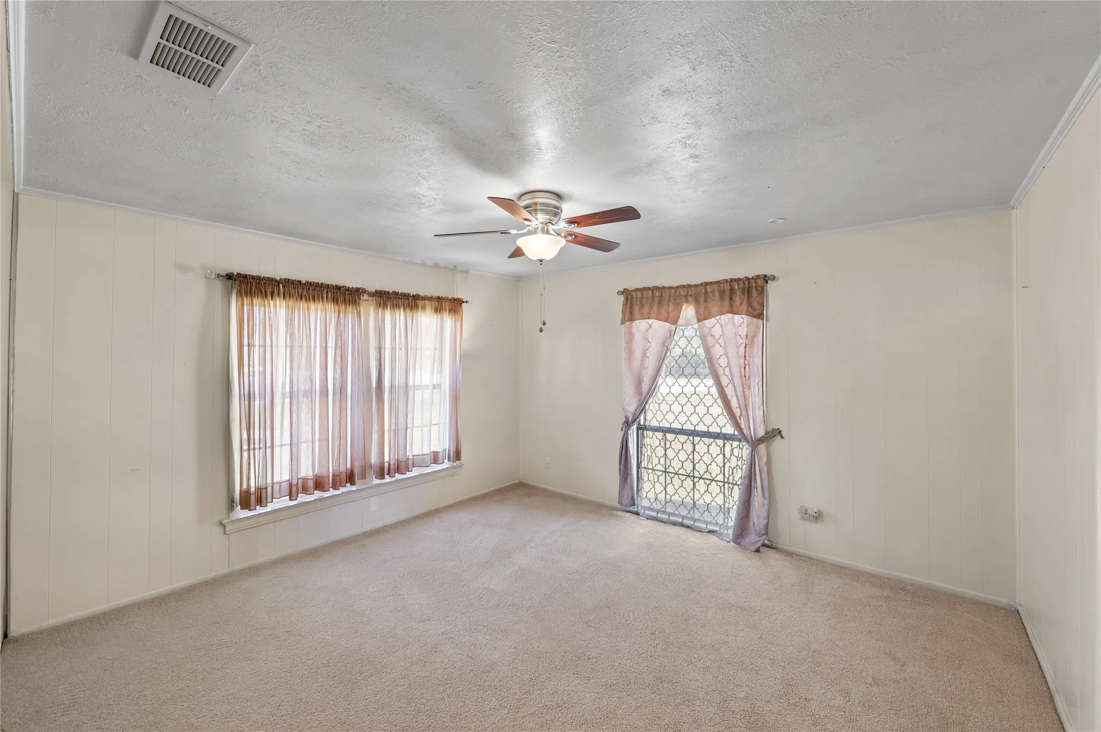 Spacious room featuring neutral carpeting, dual window sets with vertical blinds providing natural light, and a ceiling fan with integrated lighting