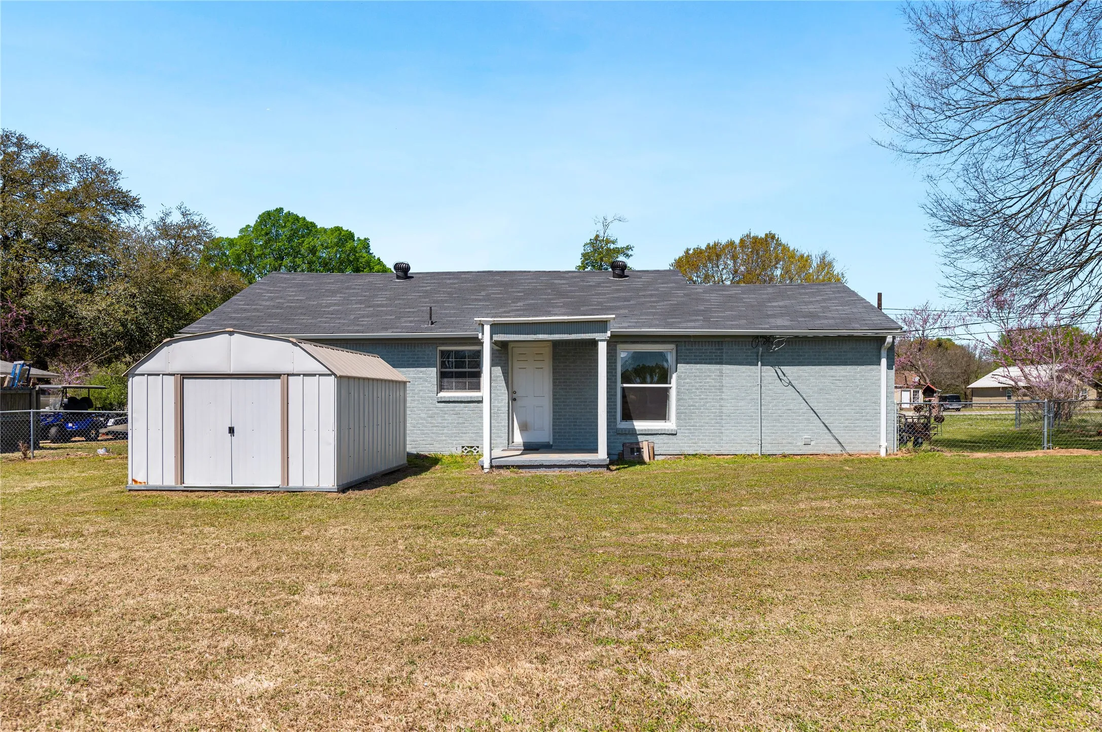 Expansive backyard featuring a gray storage shed, a covered back porch, a gray exterior with white trim, and a dark shingle roof