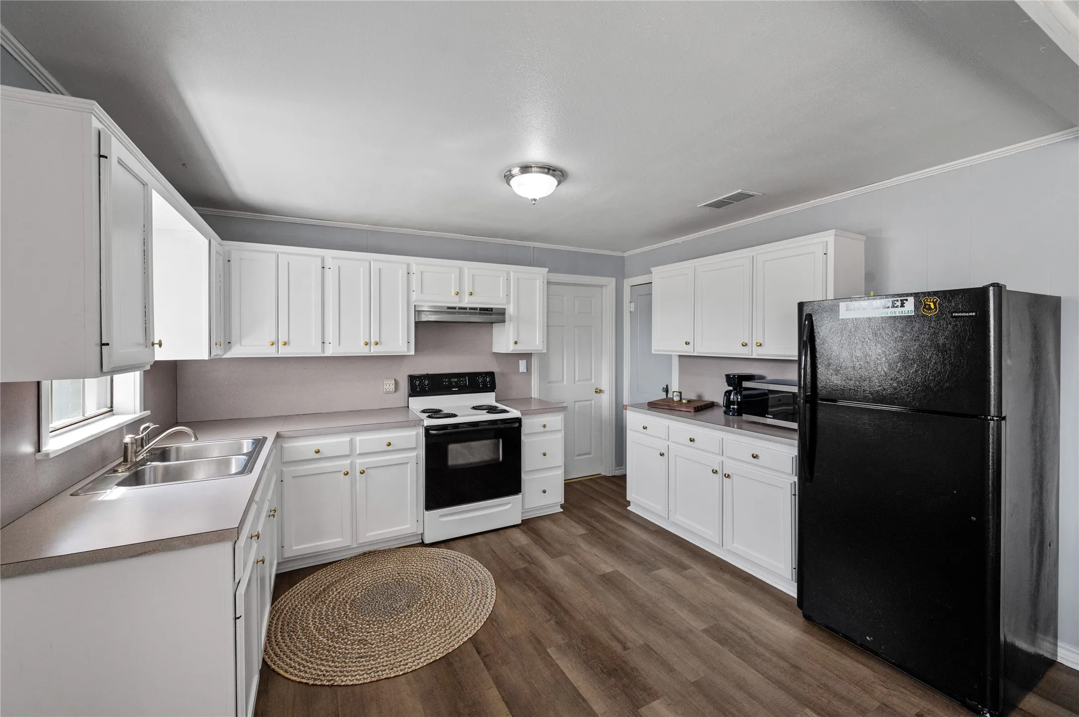 Kitchen featuring wood-finish flooring, white cabinetry with gold-tone hardware, a double basin stainless steel sink, a black electric range, and a black refrigerator