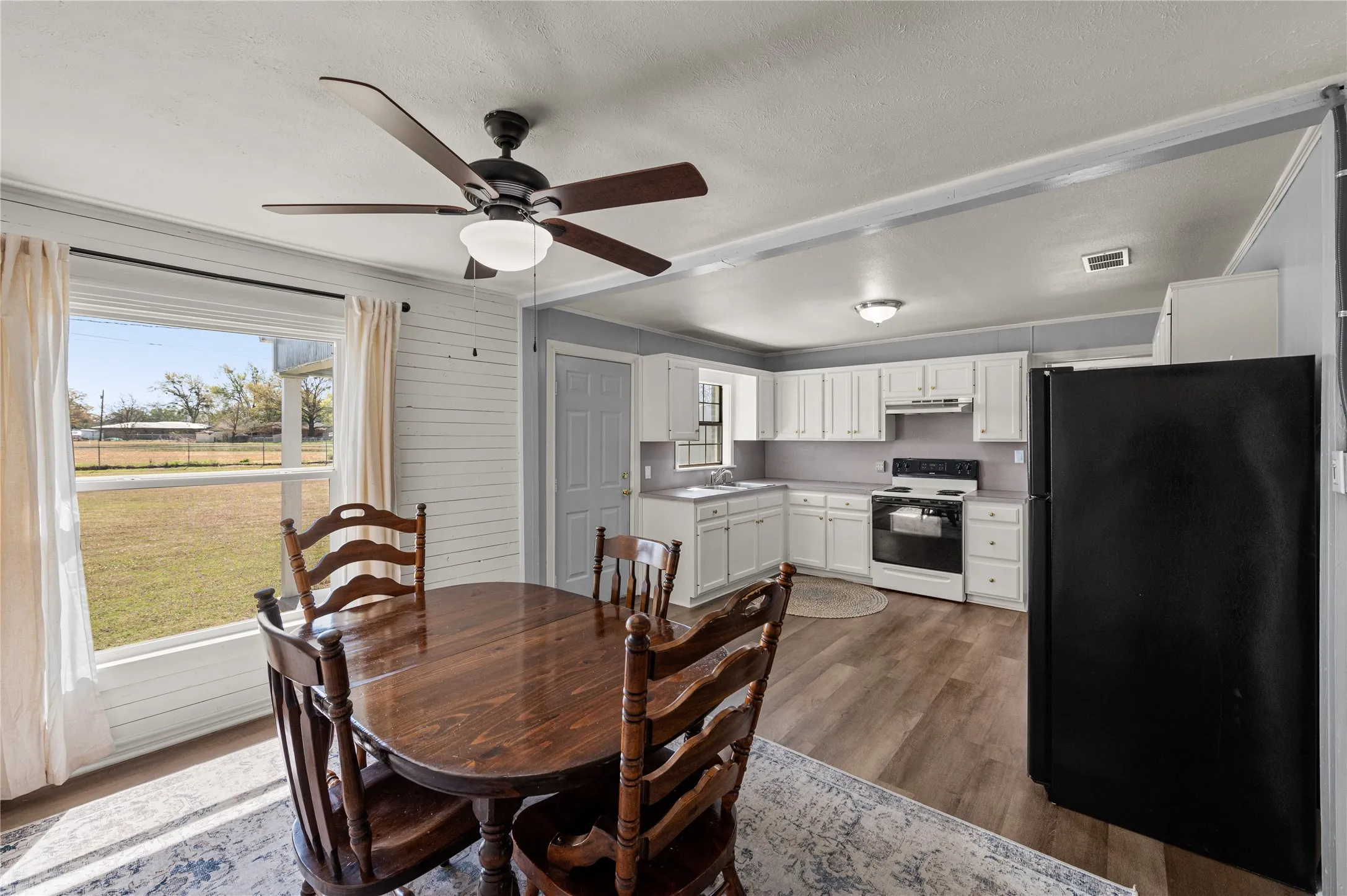 Open-concept living space with wood-finish flooring, white shiplap accent wall, and a ceiling fan