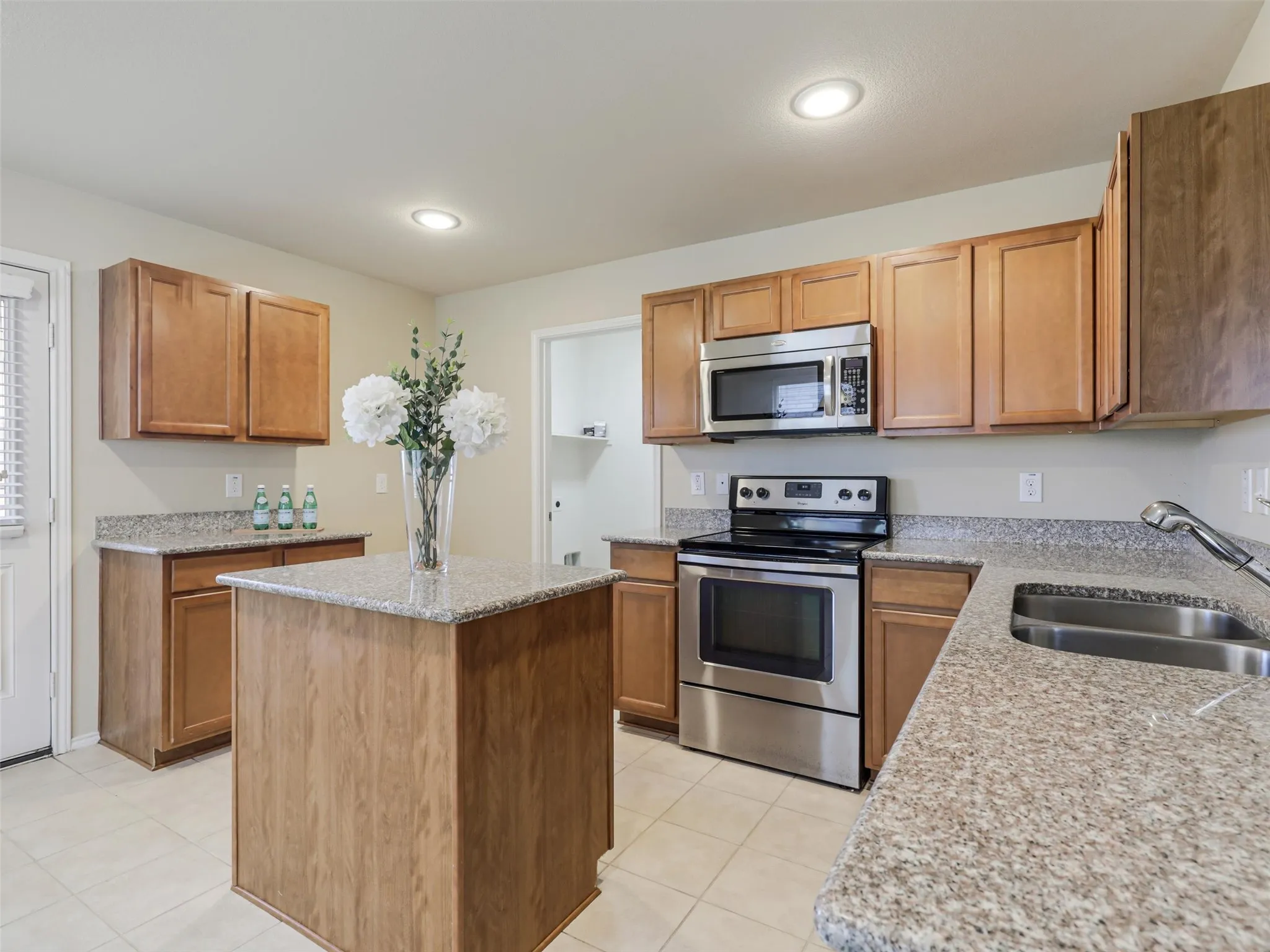 Kitchen featuring wood cabinetry, stainless steel appliances, speckled countertops, a center island, and tile flooring