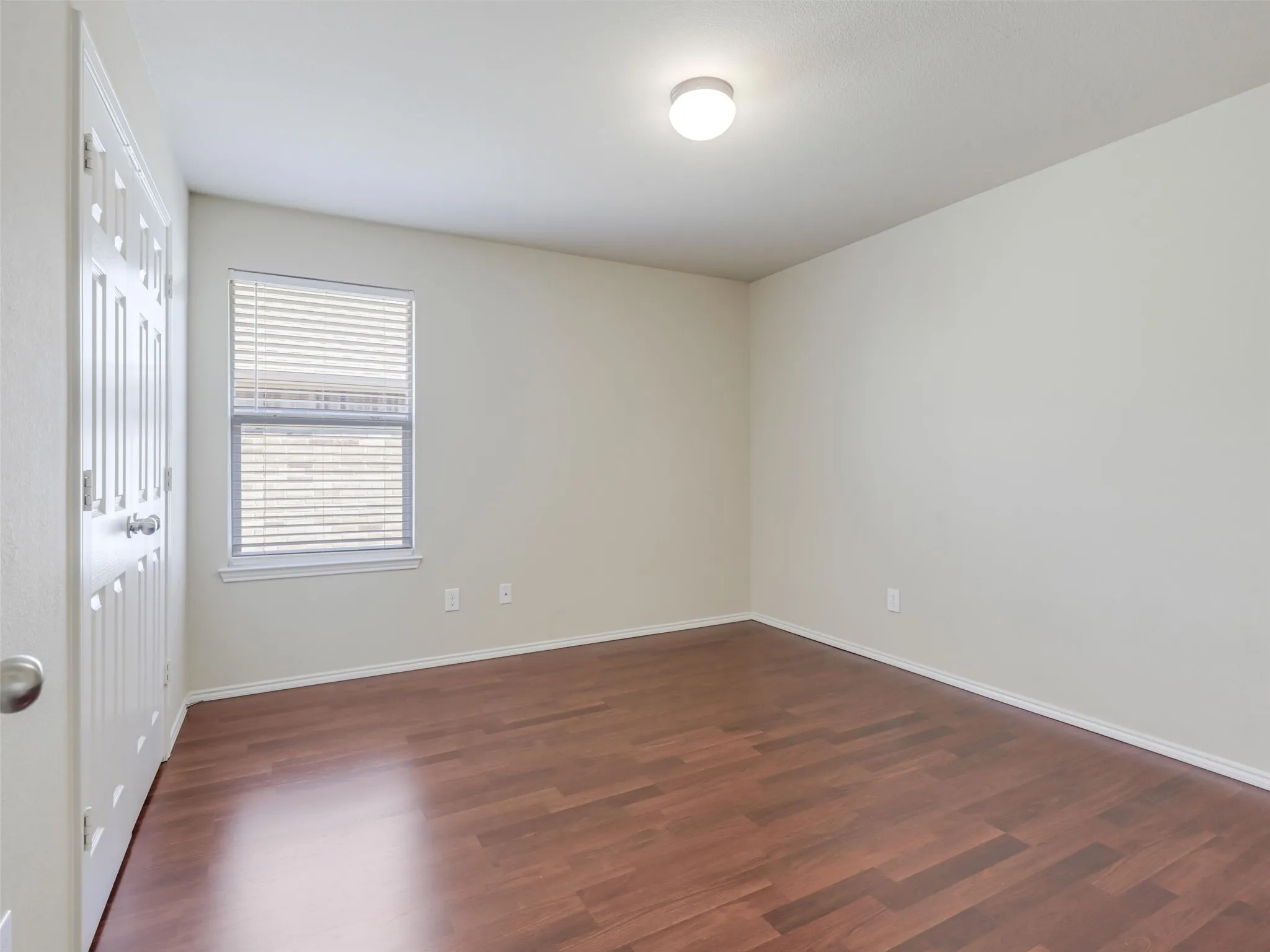 Wood-finish flooring, neutral wall tones, window with horizontal blinds, flush mount ceiling light, and a paneled door