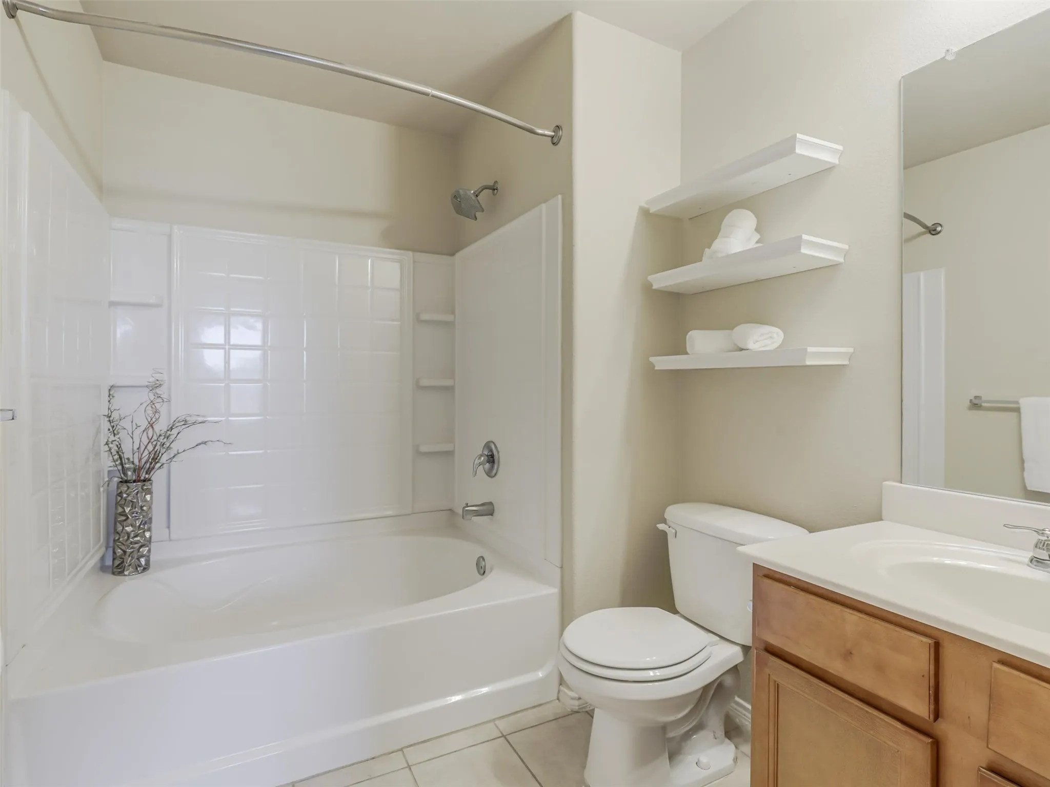 Tub and shower combination with a curved shower rod, vanity with wood-finish cabinetry, and built-in wall shelving