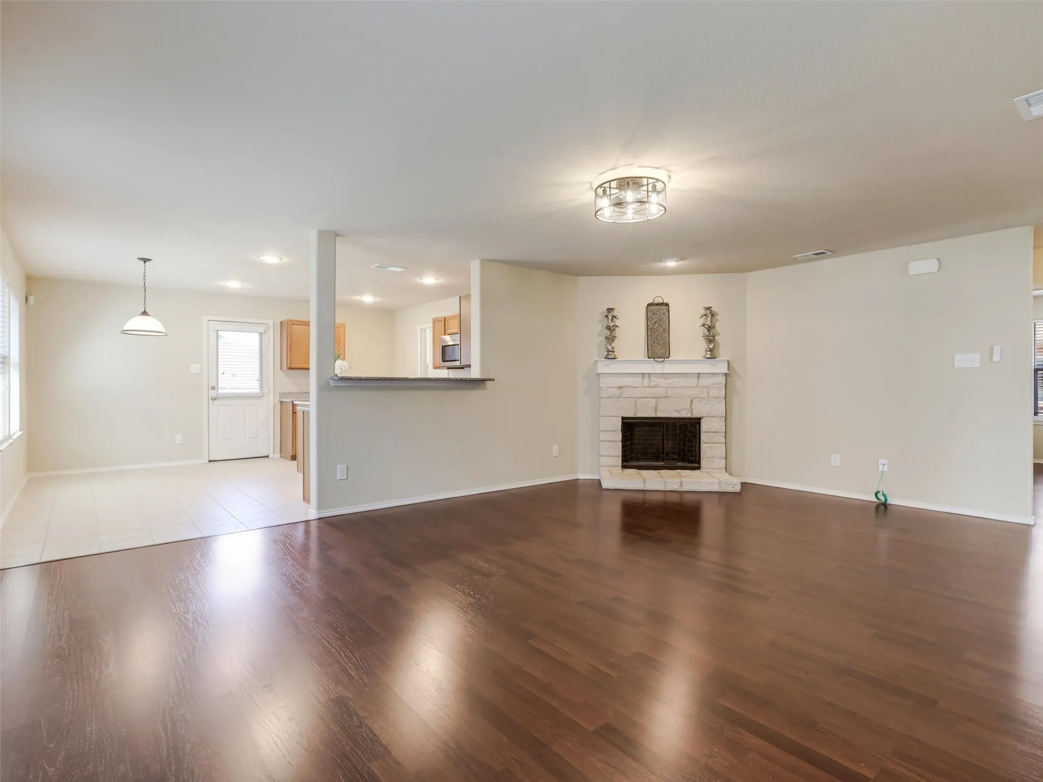 Wood-finish flooring, stone-clad fireplace, built-in breakfast bar, kitchen with light wood cabinetry, and tile flooring