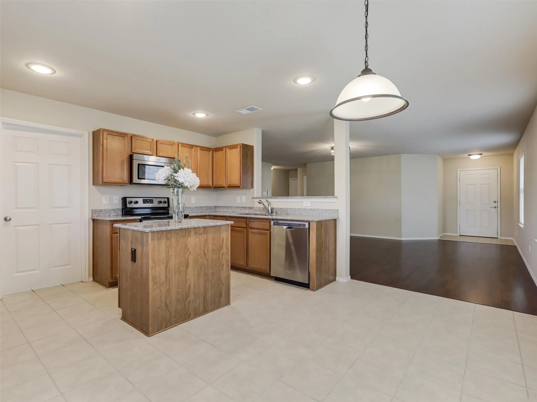 Kitchen featuring a center island, wood cabinetry, granite-style countertops, stainless steel appliances, and tile flooring