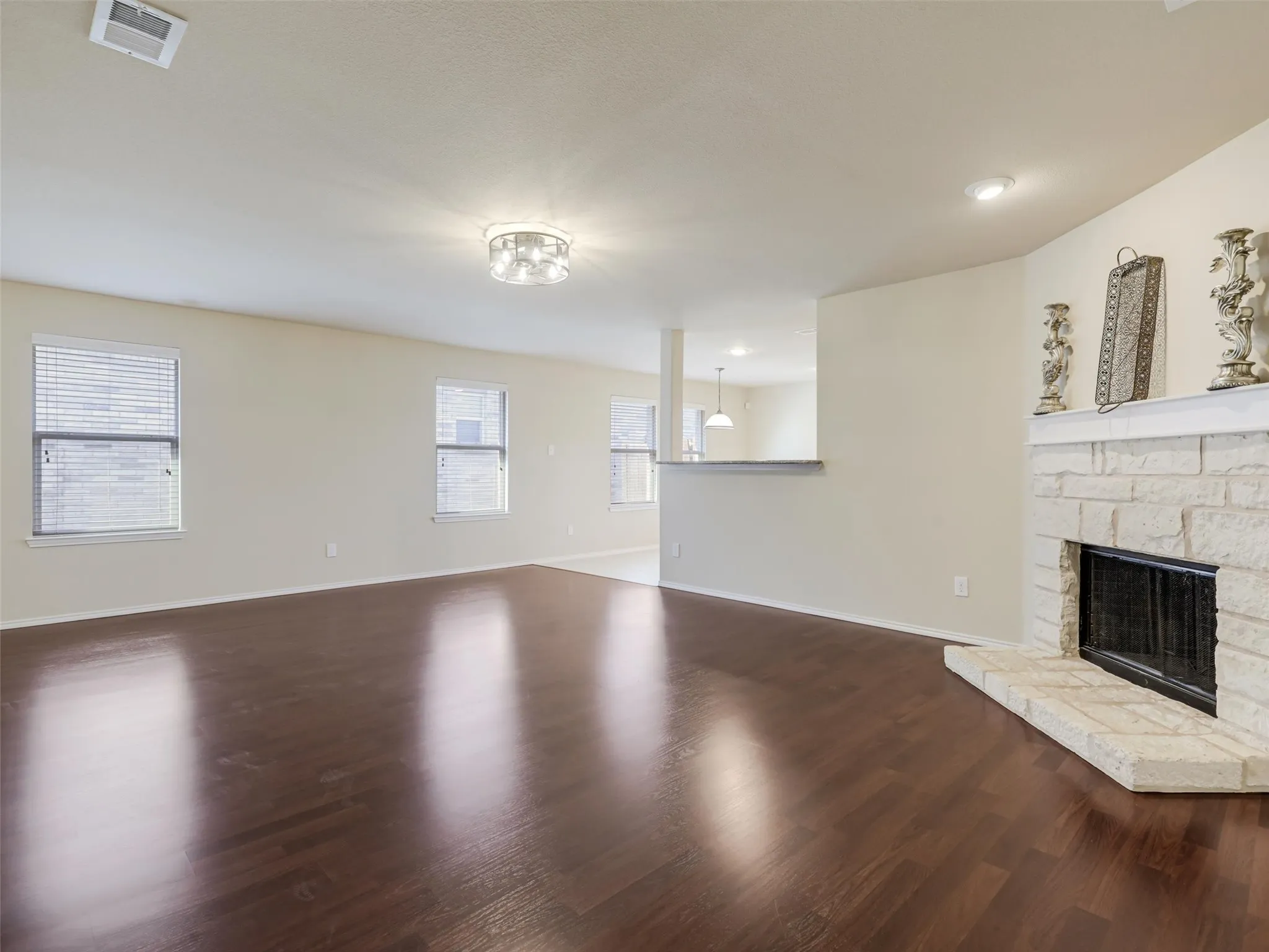 Expansive living area with wood-finish flooring, a stone-clad fireplace with hearth, multiple windows, and recessed lighting